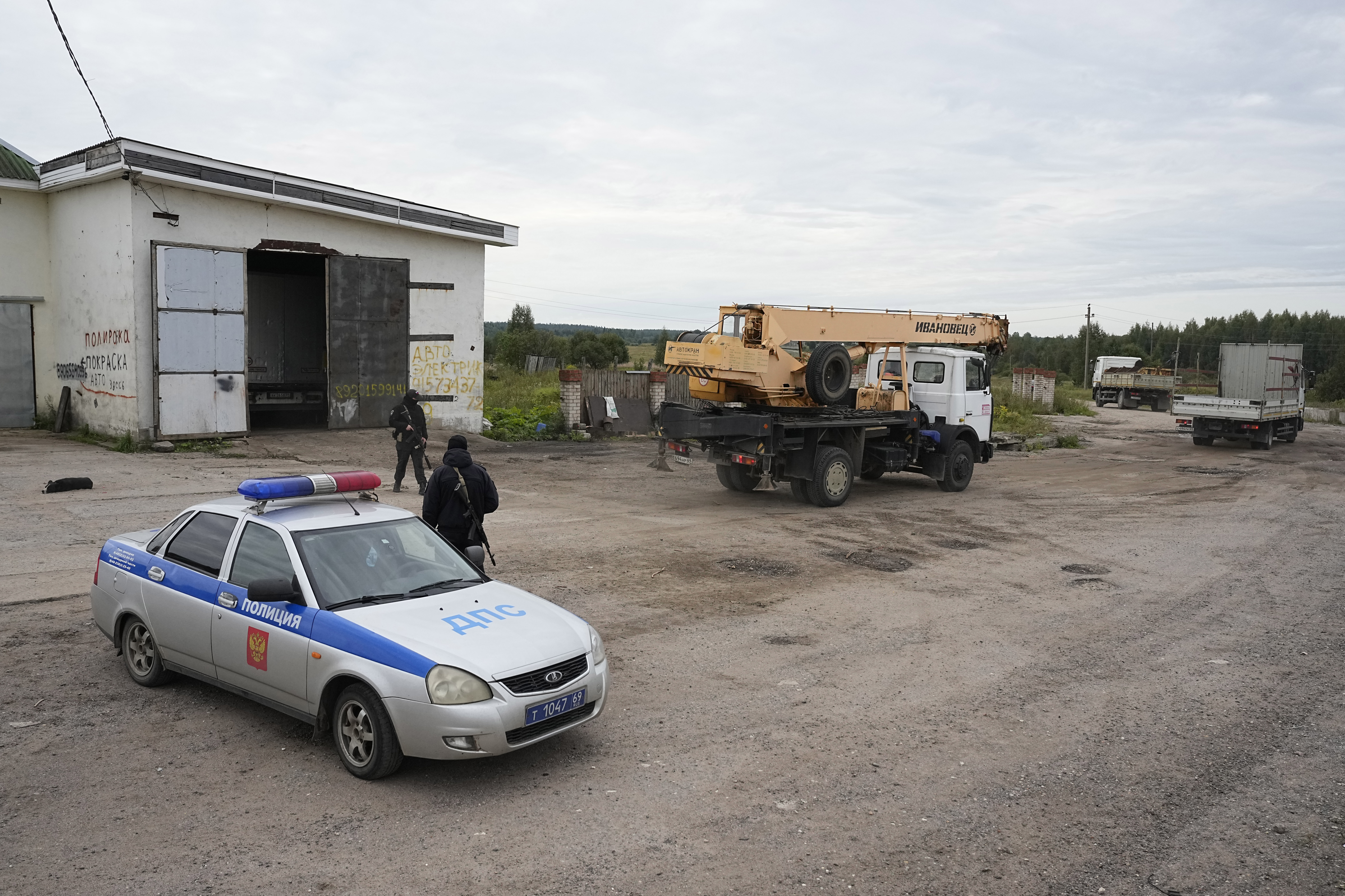 Trucks and a crane arrive as Russian servicemen guard a road leading to the private jet crash site, near the village of Kuzhenkino, Tver region, Russia, Friday, Aug. 25, 2023 