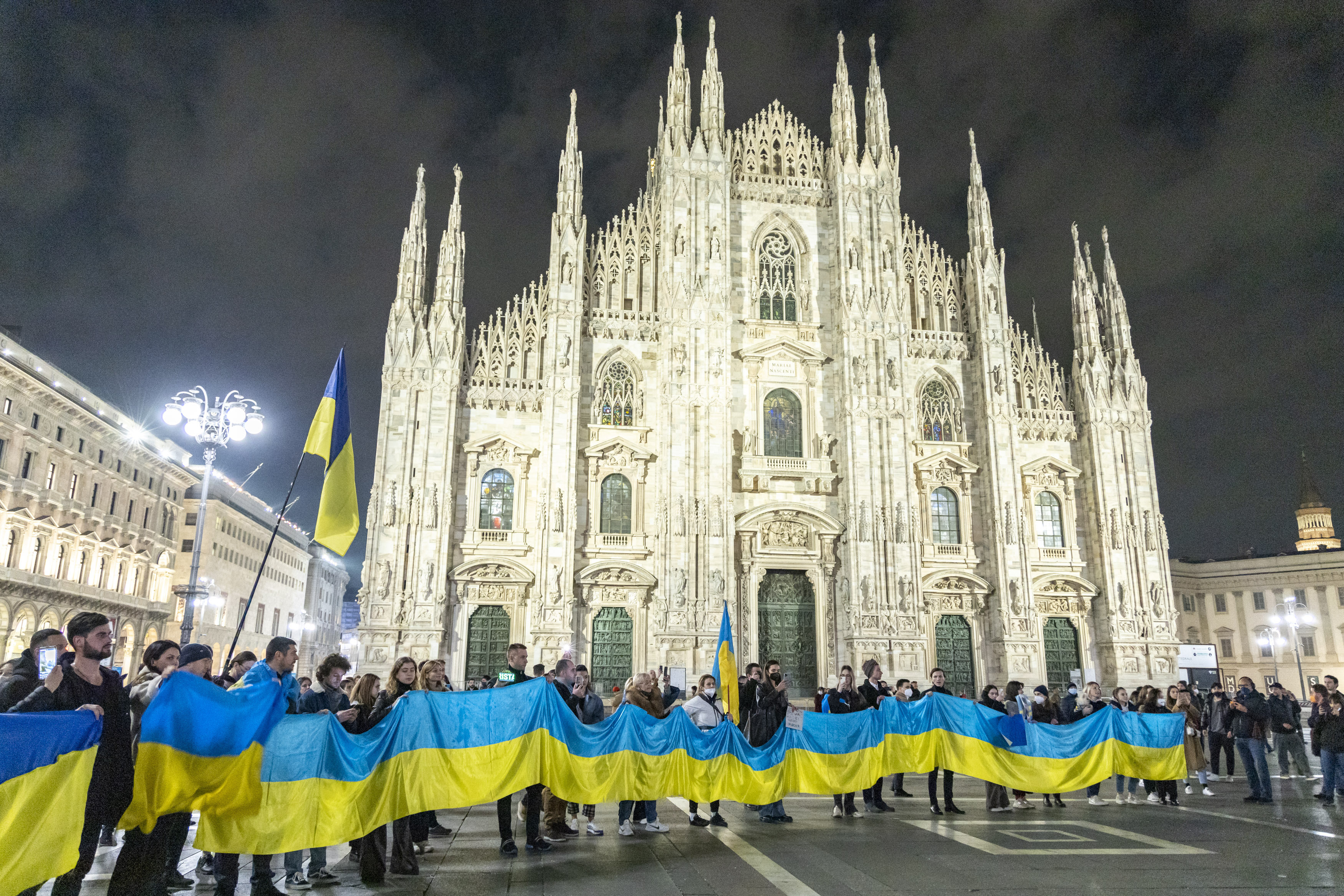 People hold a large flag of Ukraine in Duomo Square, Milan, Italy, Thursday Feb. 24, 2022.