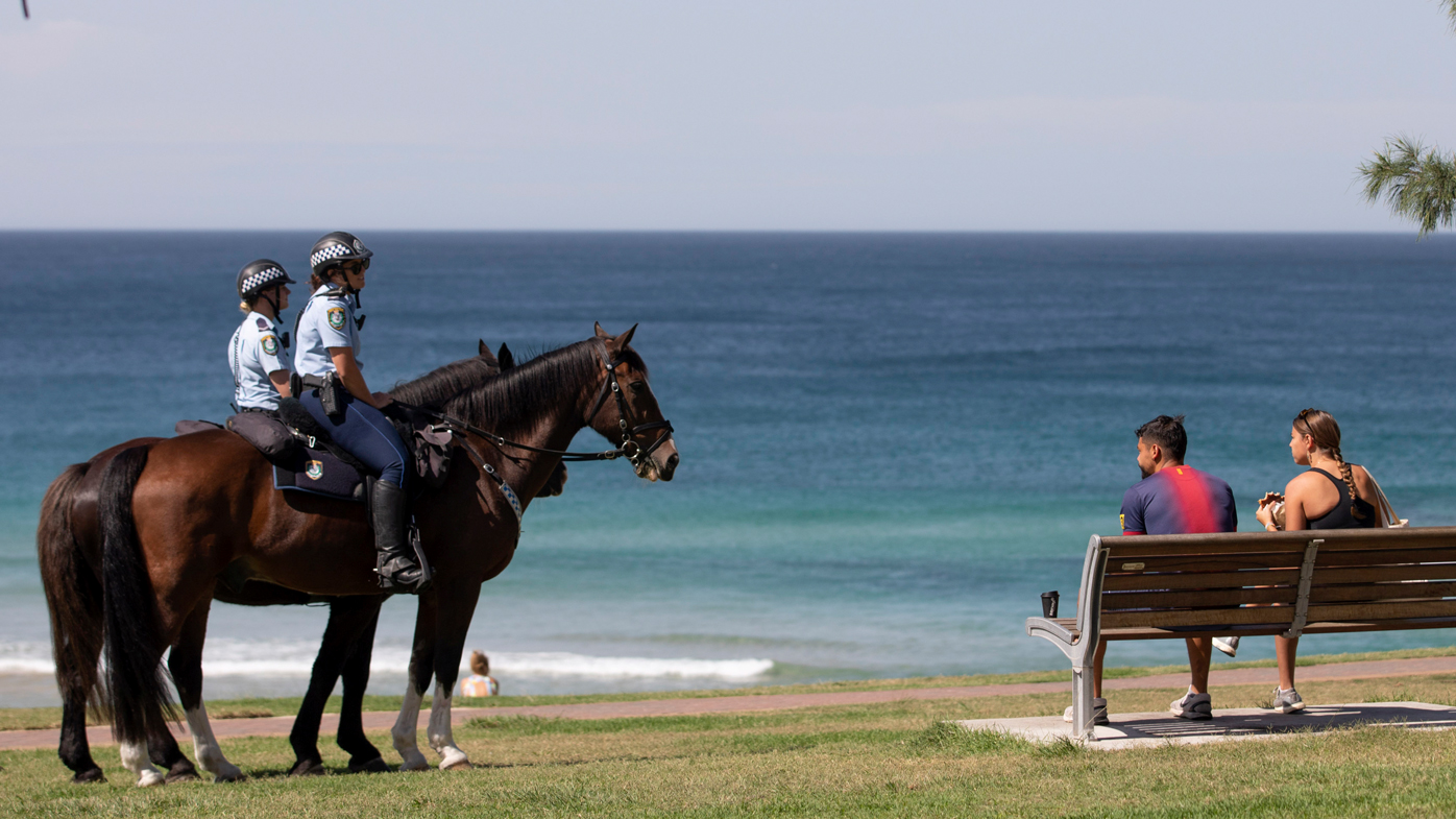 Mounted police patrol a mostly empty Bondi Beach and speak to people about  NSW social distancing laws. 