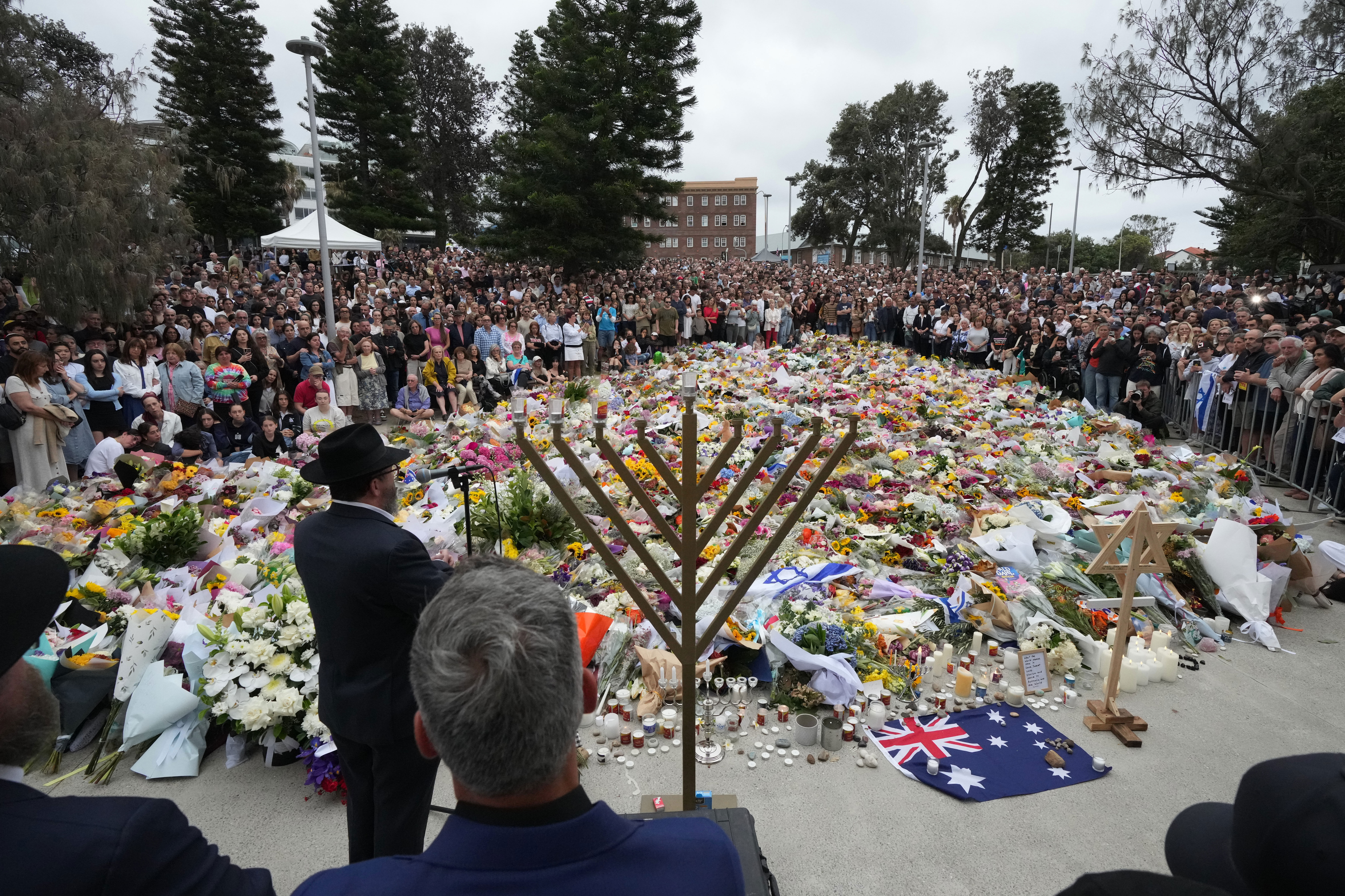 Rabbi Motti Feldman, lower left, speaks at a menorah lighting ceremony at a floral memorial for victims of Sunday's shooting, at the Bondi Pavilion.