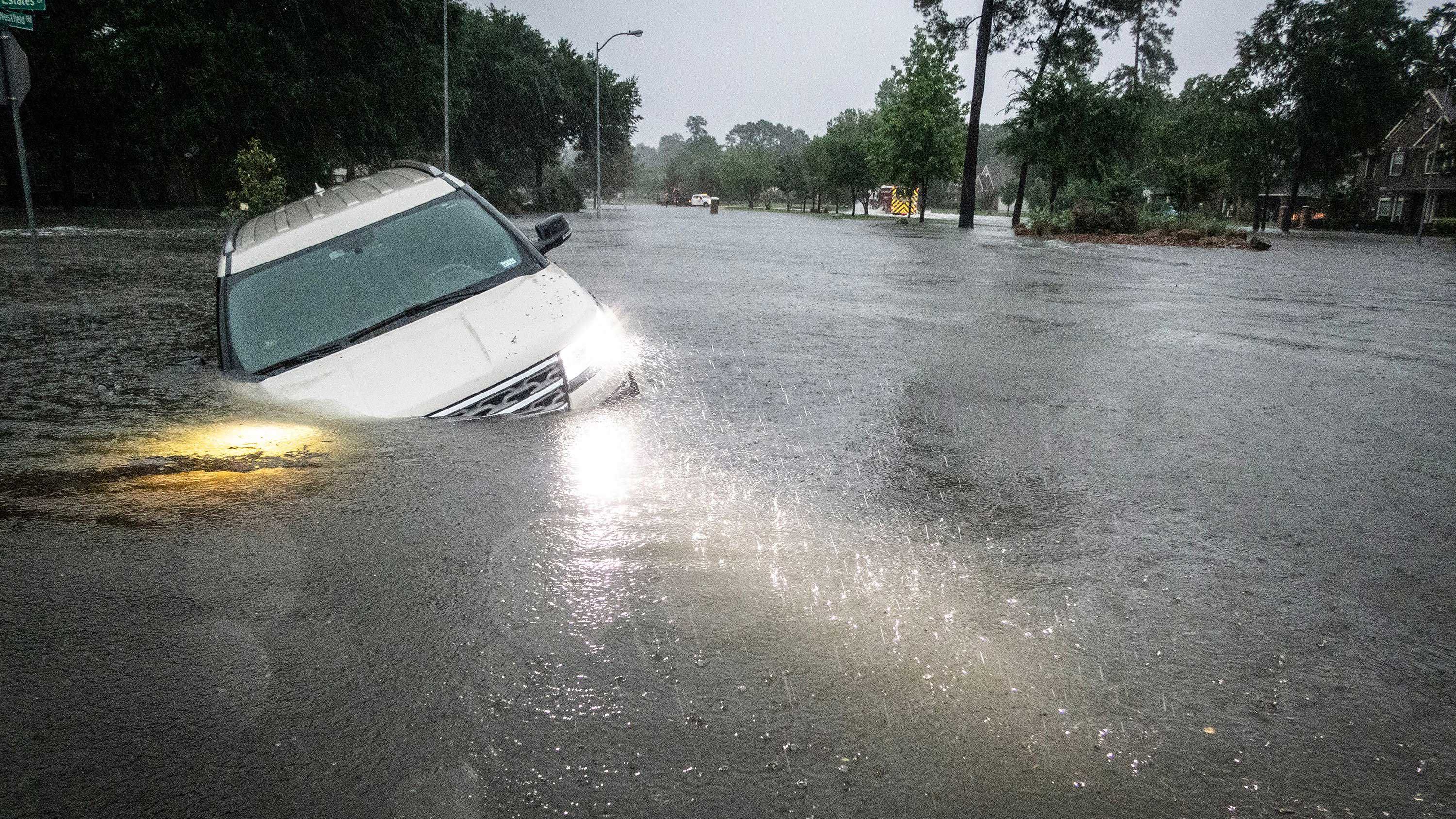 An SUV is stranded in a ditch along a stretch of street flooding during a severe storm Thursday in Spring, Texas.