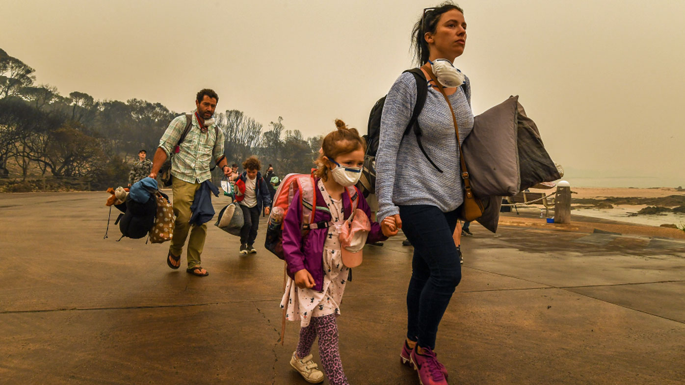 A child in a face mask clutches her mum's hand as they evacuate Mallacoota.