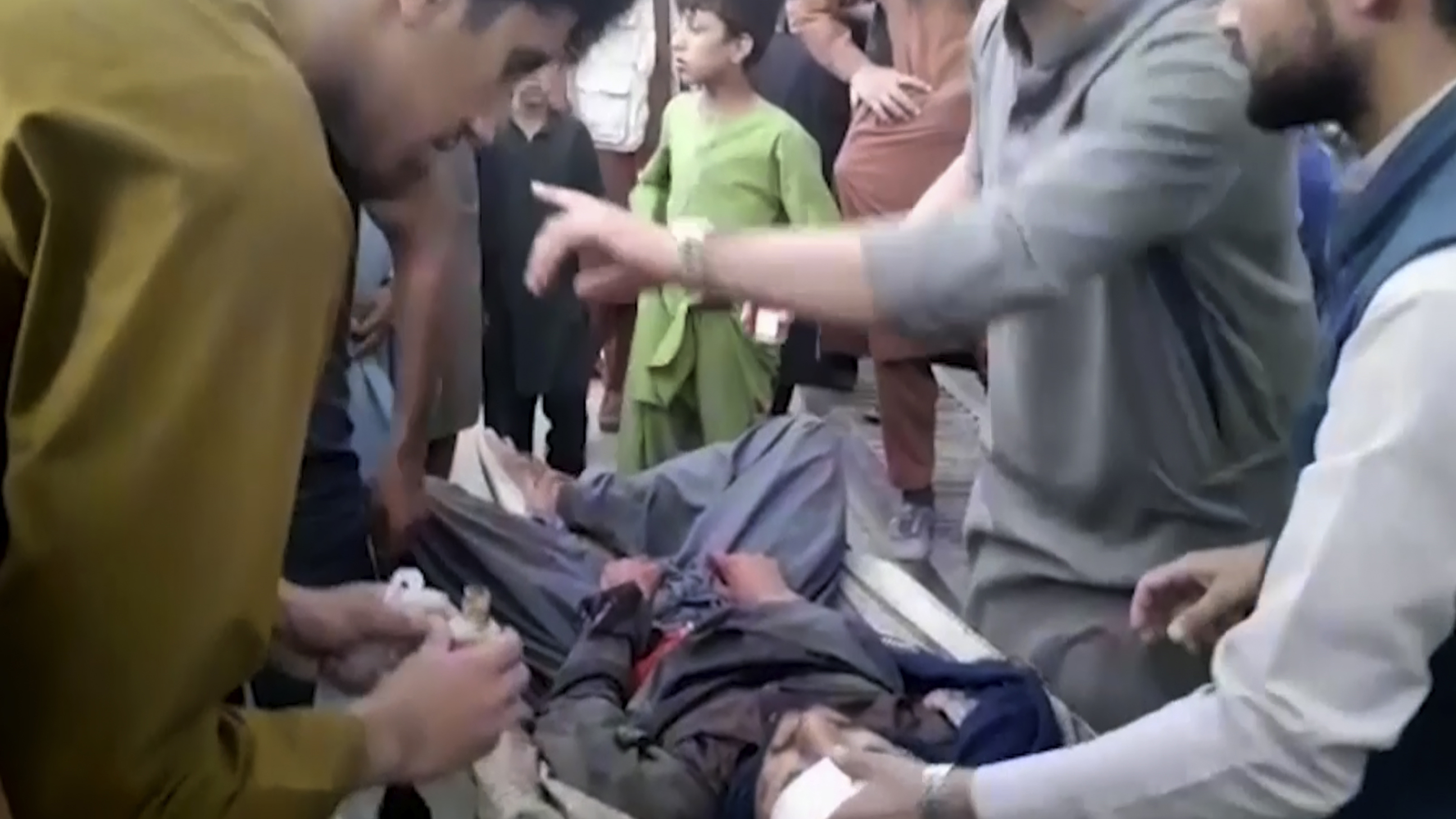In this frame grab from video, people attend to a wounded man near the site of a deadly explosion outside the airport in Kabul, Afghanistan.