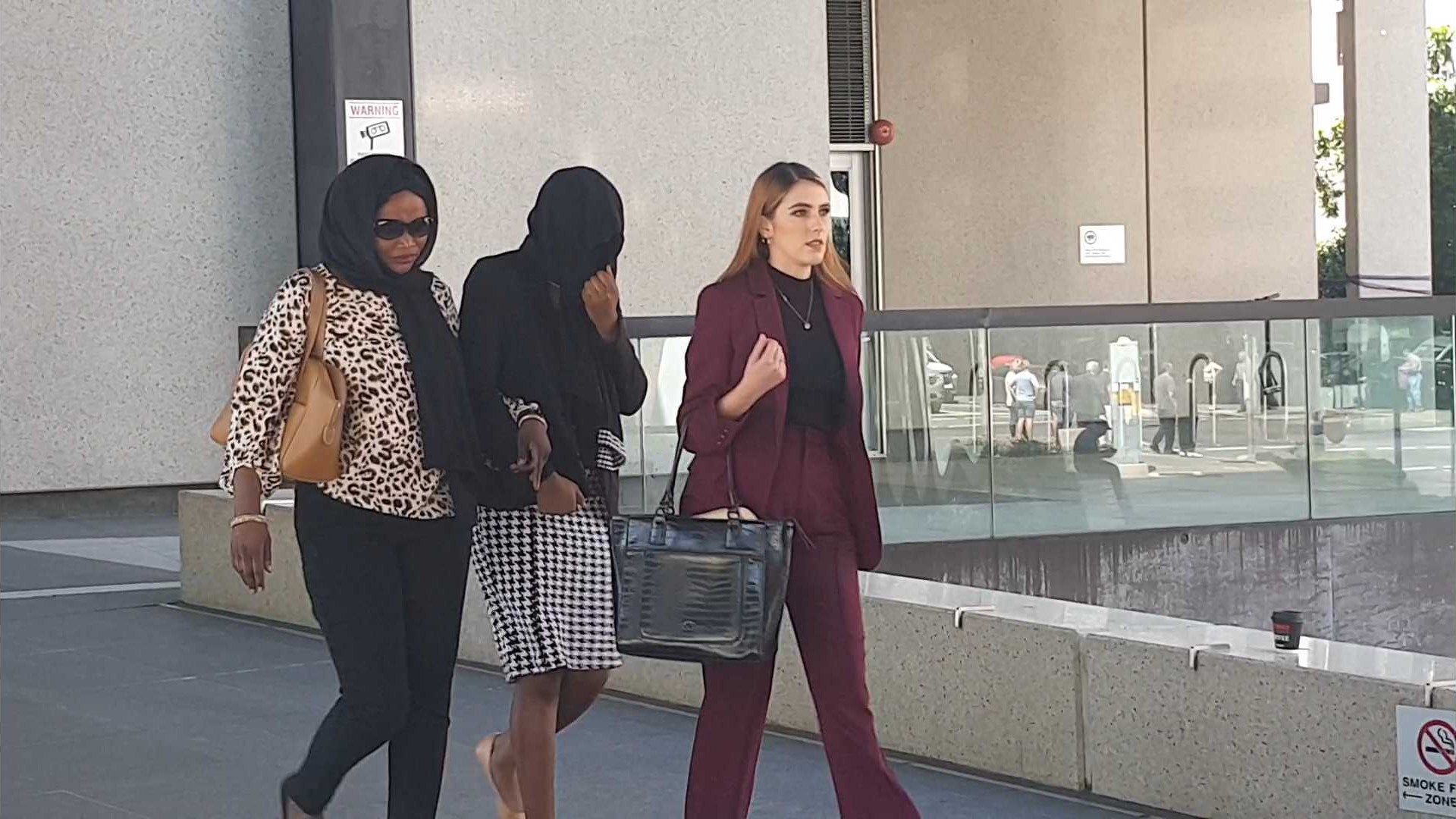 Diana Lasu leaves Brisbane Magistrates Court covering her face and linking arms with her mother.