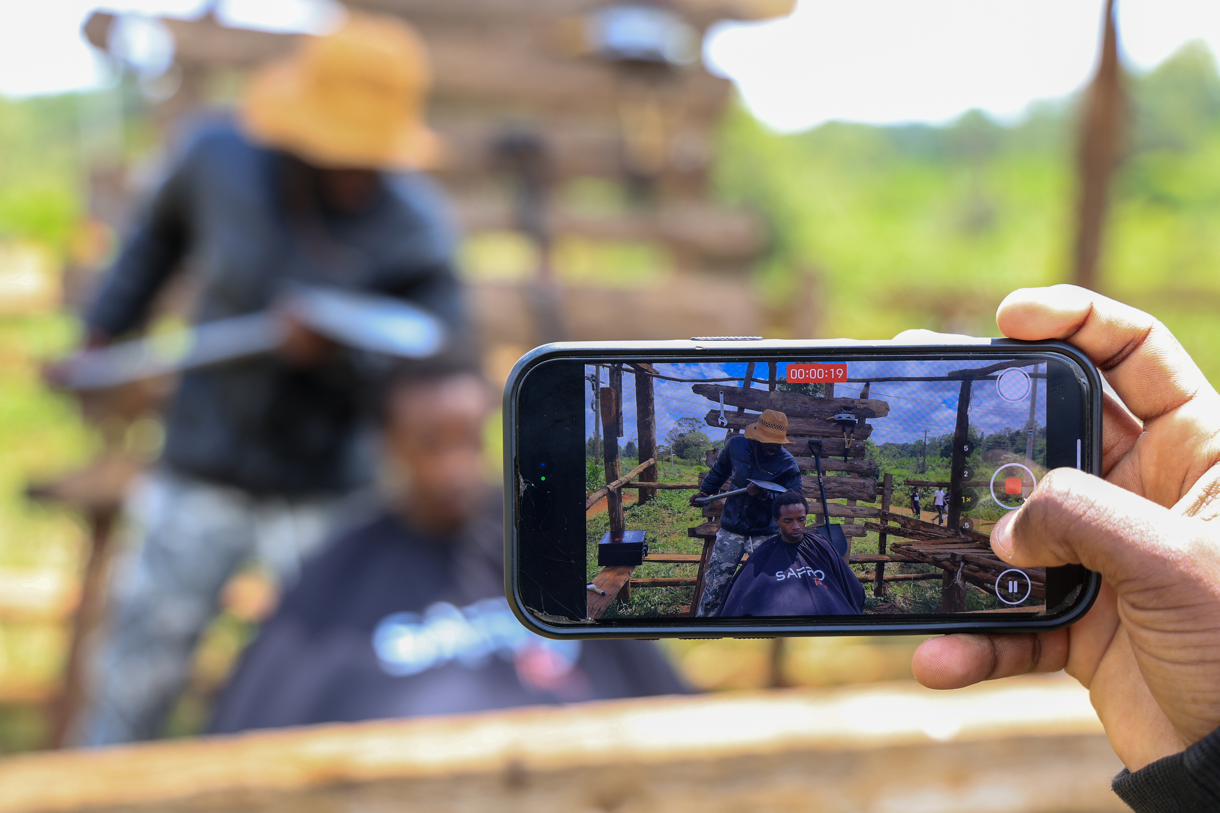 A man uses his phone to record barber and content creator Safari Martins as he shaves Ian Njenga in Kiambu, Kenya, Wednesday, Nov. 26, 2025. (AP Photo/Andrew Kasuku)