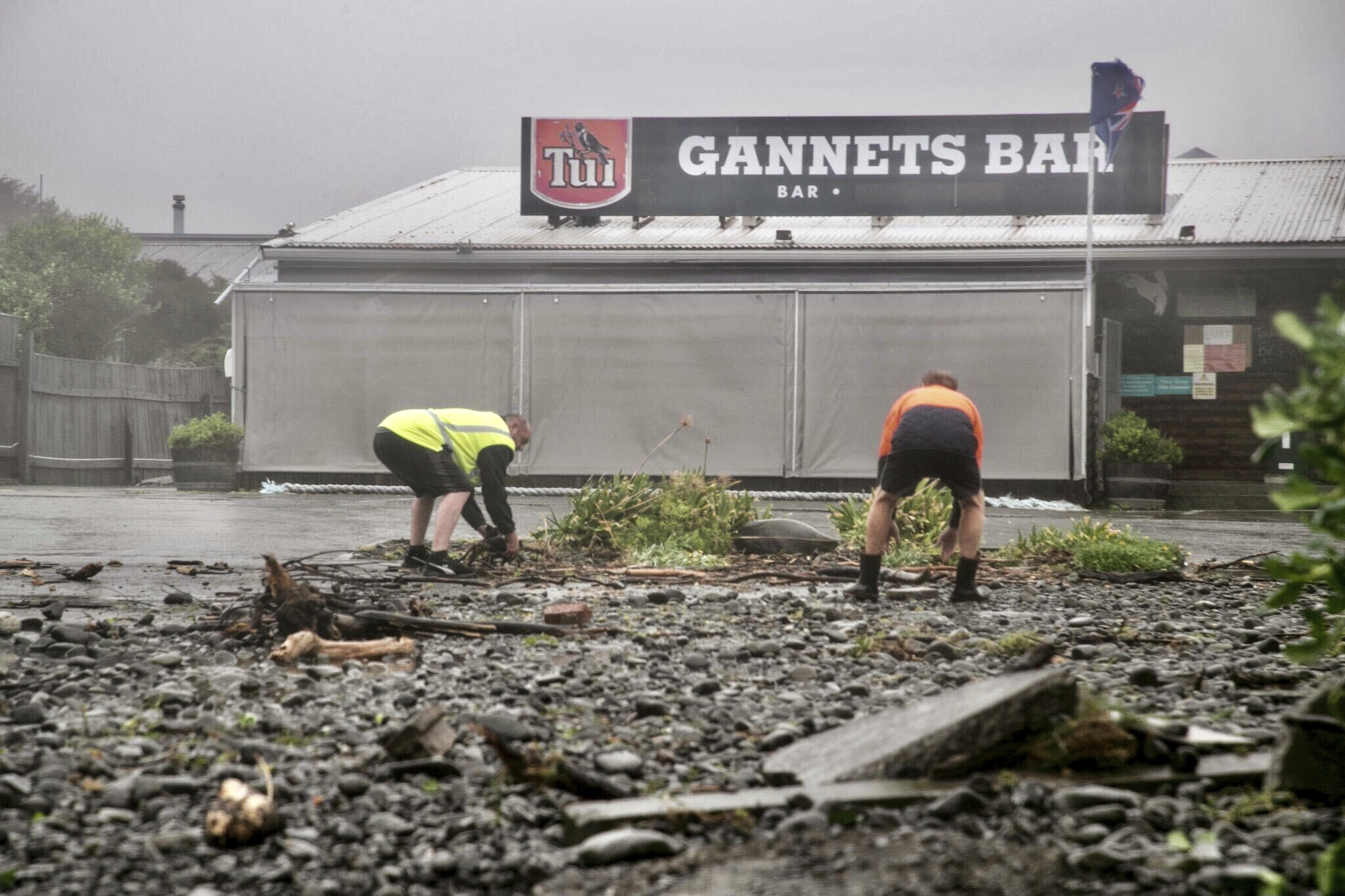 Men clear debris by hand on a flooded road in Te Awanga, southeast of Auckland, New Zealand, Tuesday, Feb. 14, 2023.
