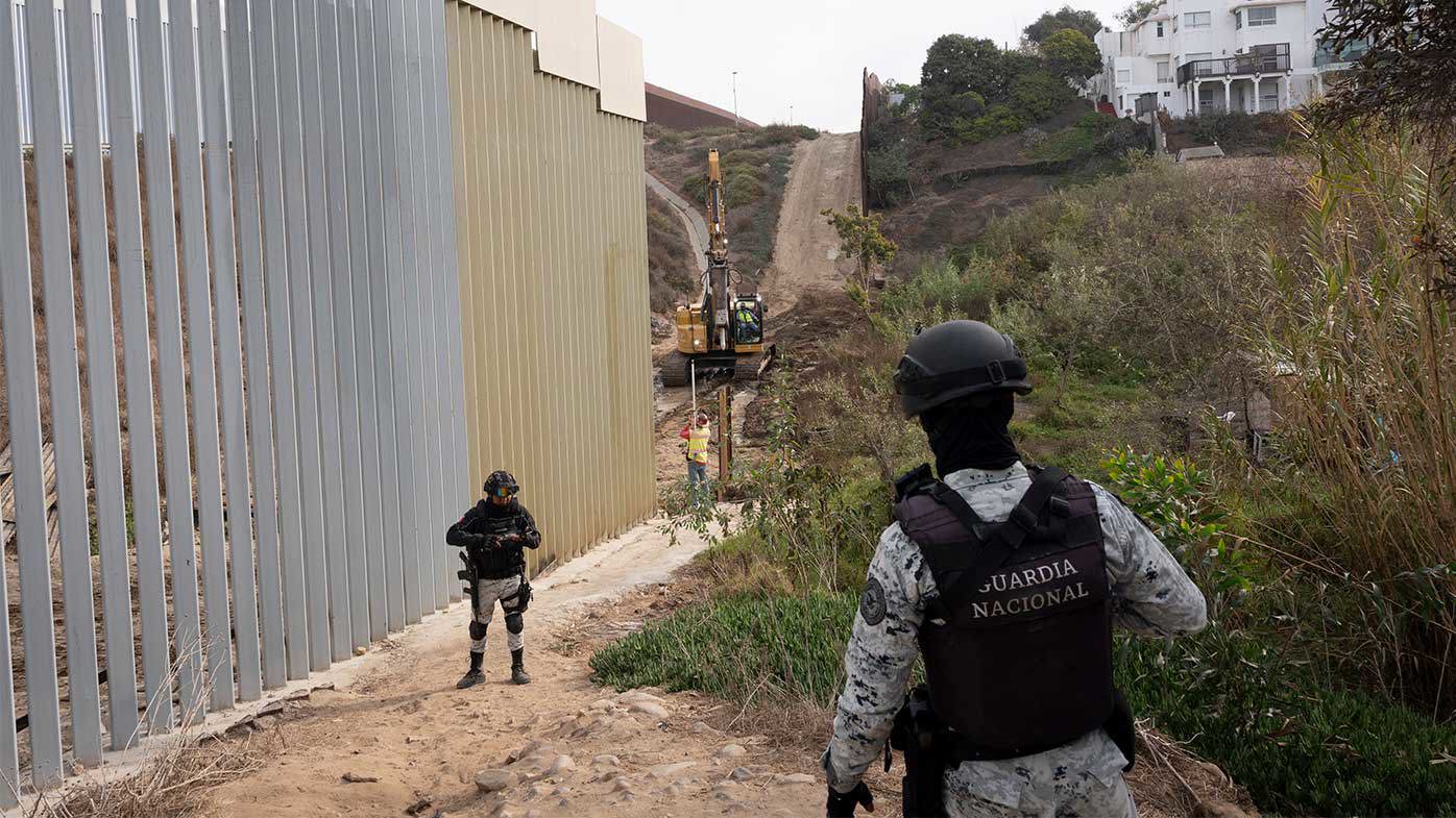 Los miembros de la Guardia Nacional Mexicana observan cómo se actualiza una sección de la cerca fronteriza.