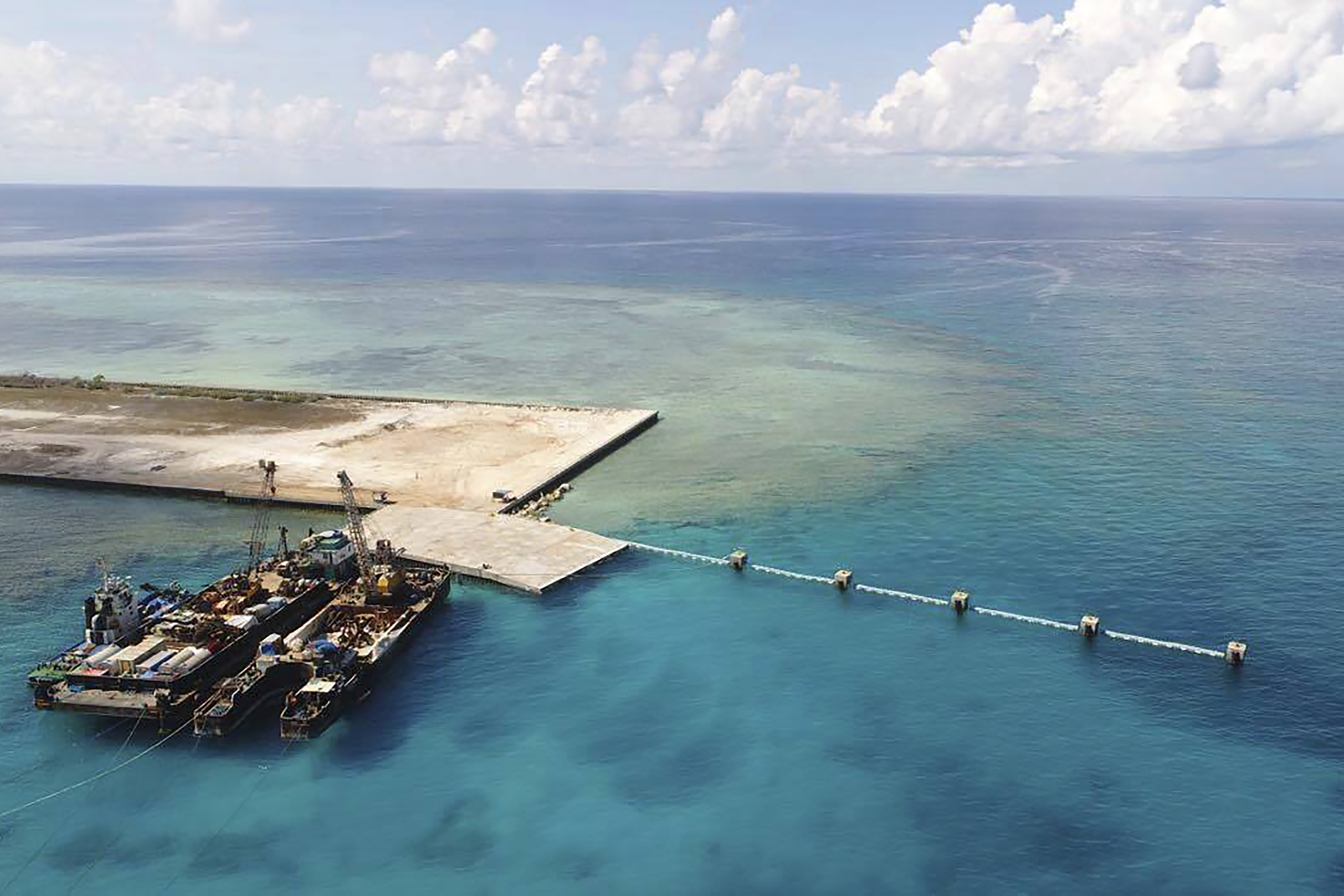 In this photo provided by the Department of National Defense, ships carrying construction materials are docked at the newly built beach ramp at the Philippine-claimed island of Thitu, in the disputed South China Sea, June 9, 2020.