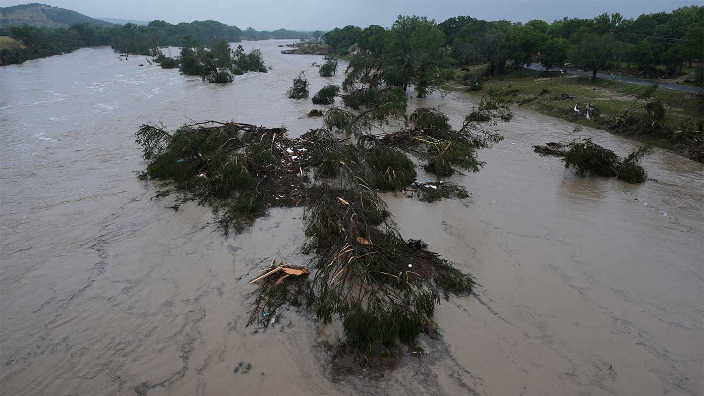 A raging Guadalupe River leaves fallen trees and debris in its wake.