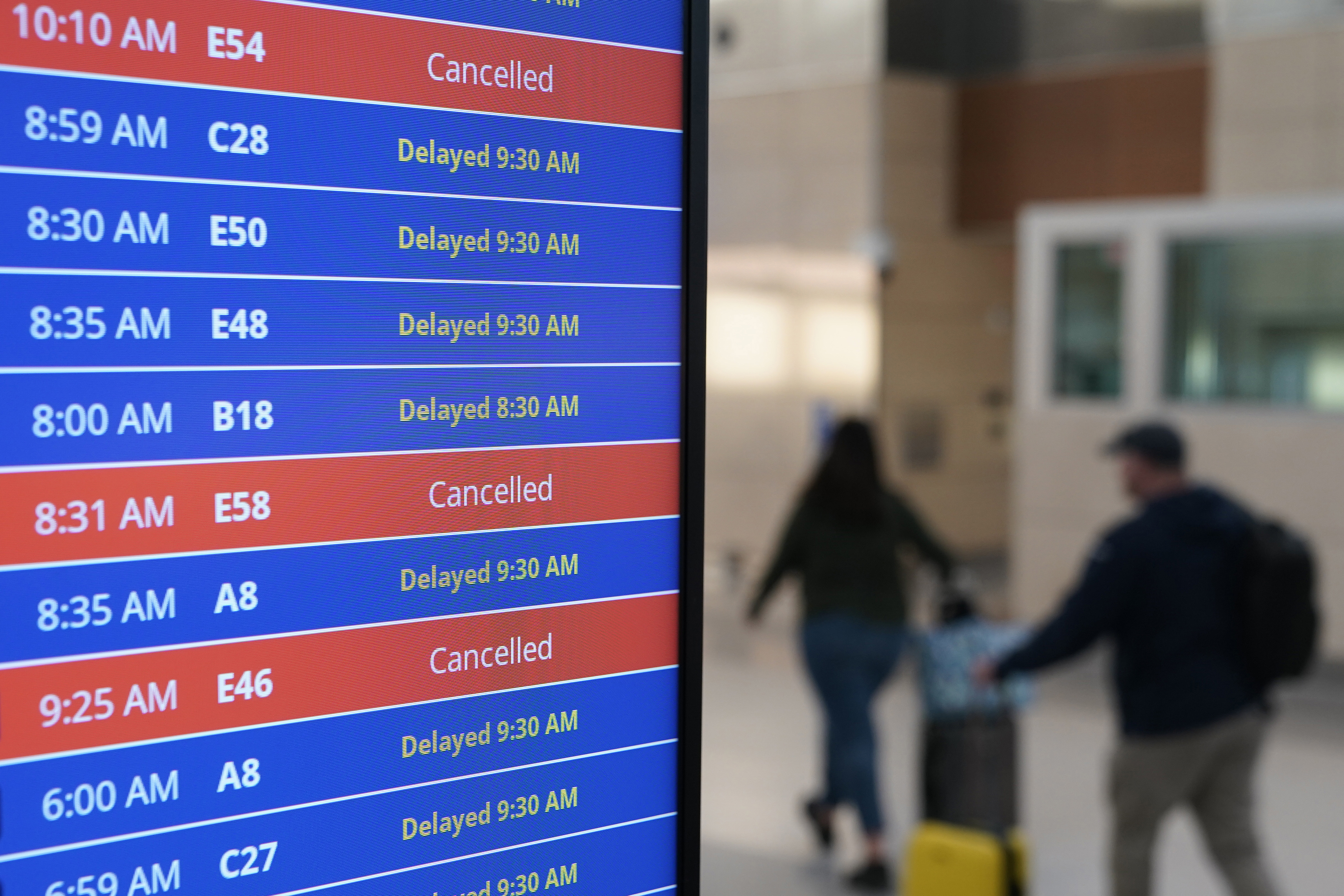 Los viajeros caminan mientras un panel de video muestra retrasos y cancelaciones de vuelos en el Aeropuerto Nacional Ronald Reagan de Washington en Arlington, Virginia, el miércoles 11 de enero de 2023.