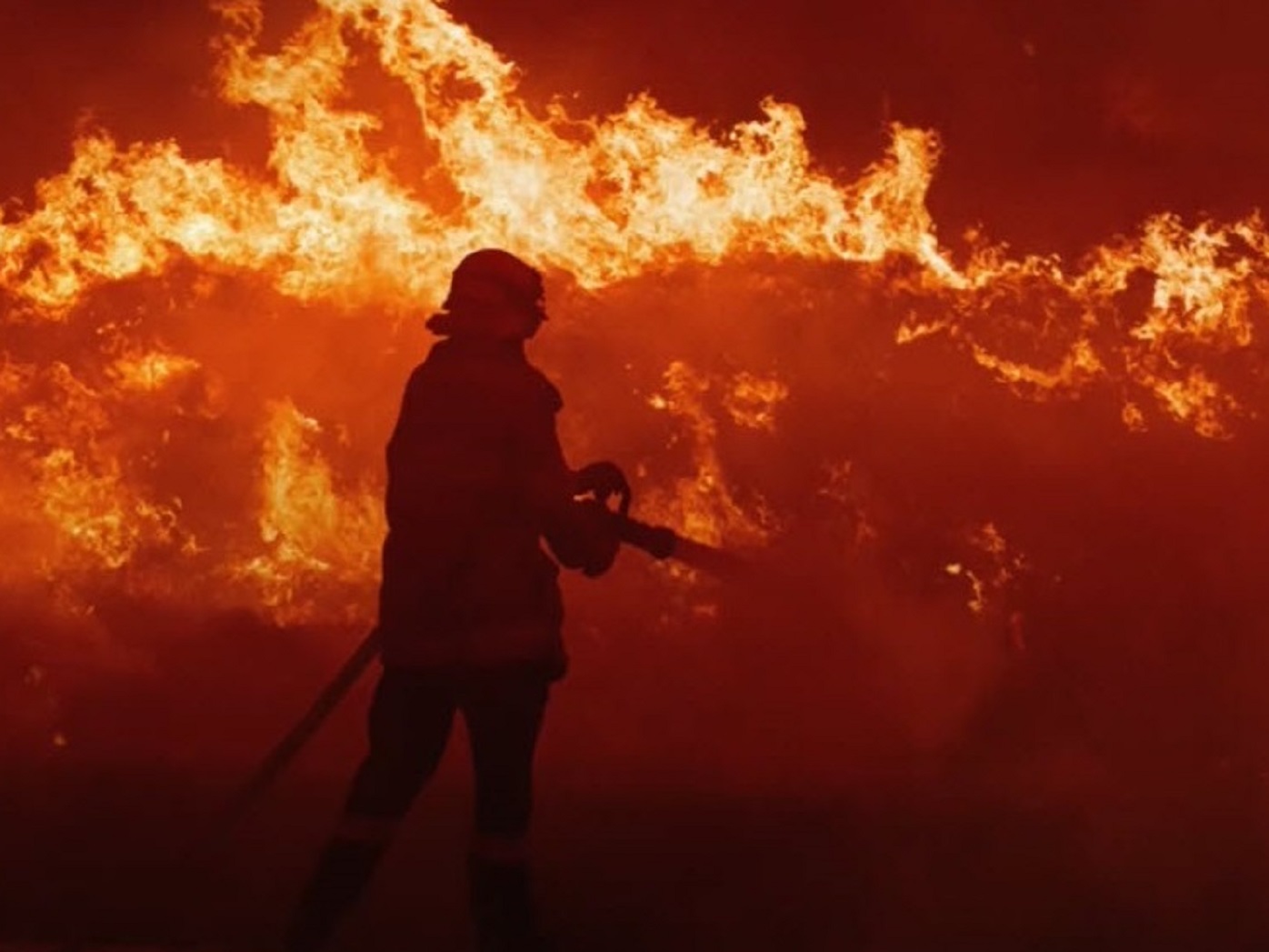 A firefighter stands in the face of a raging fire.