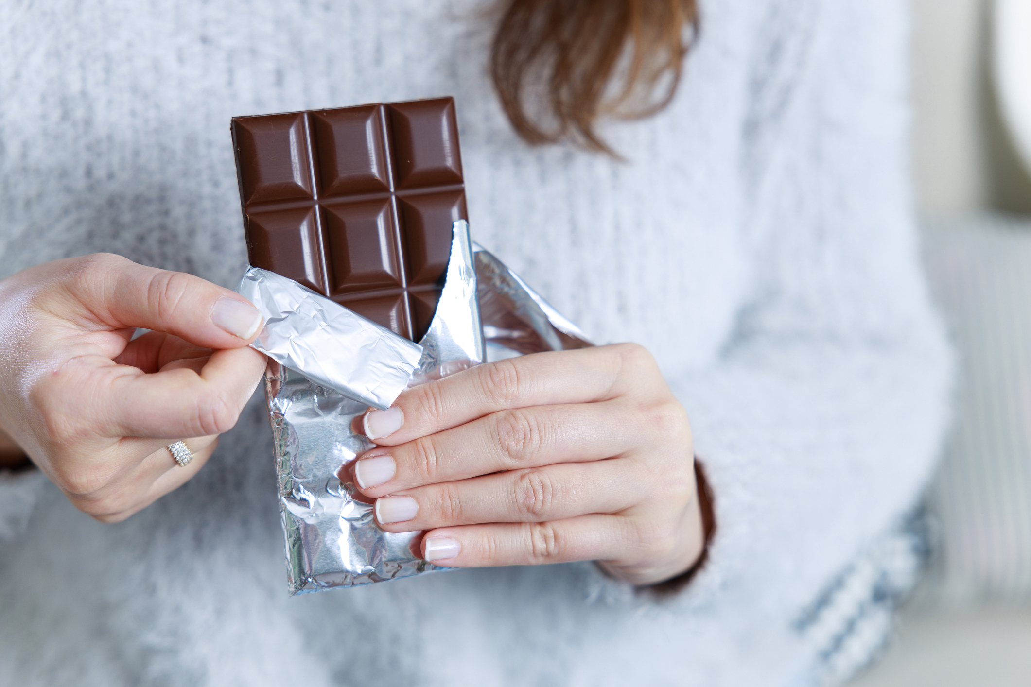 Hands of a woman holding a tile of chocolate. Chocolate bar in silver foil in woman's hand stock image