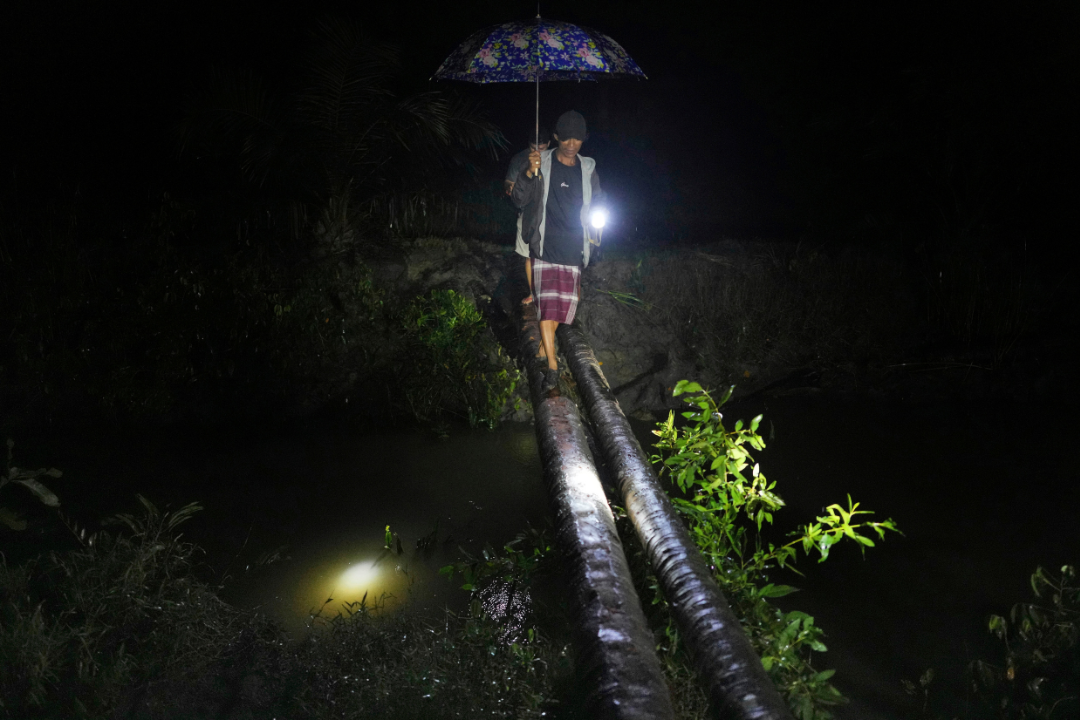 Sudirman, front, and Irfan walk on a makeshift bridge as they inspect their fish and shrimp ponds in Budong-Budong, West Sulawesi Island, Indonesia, Monday, Feb. 24, 2025.