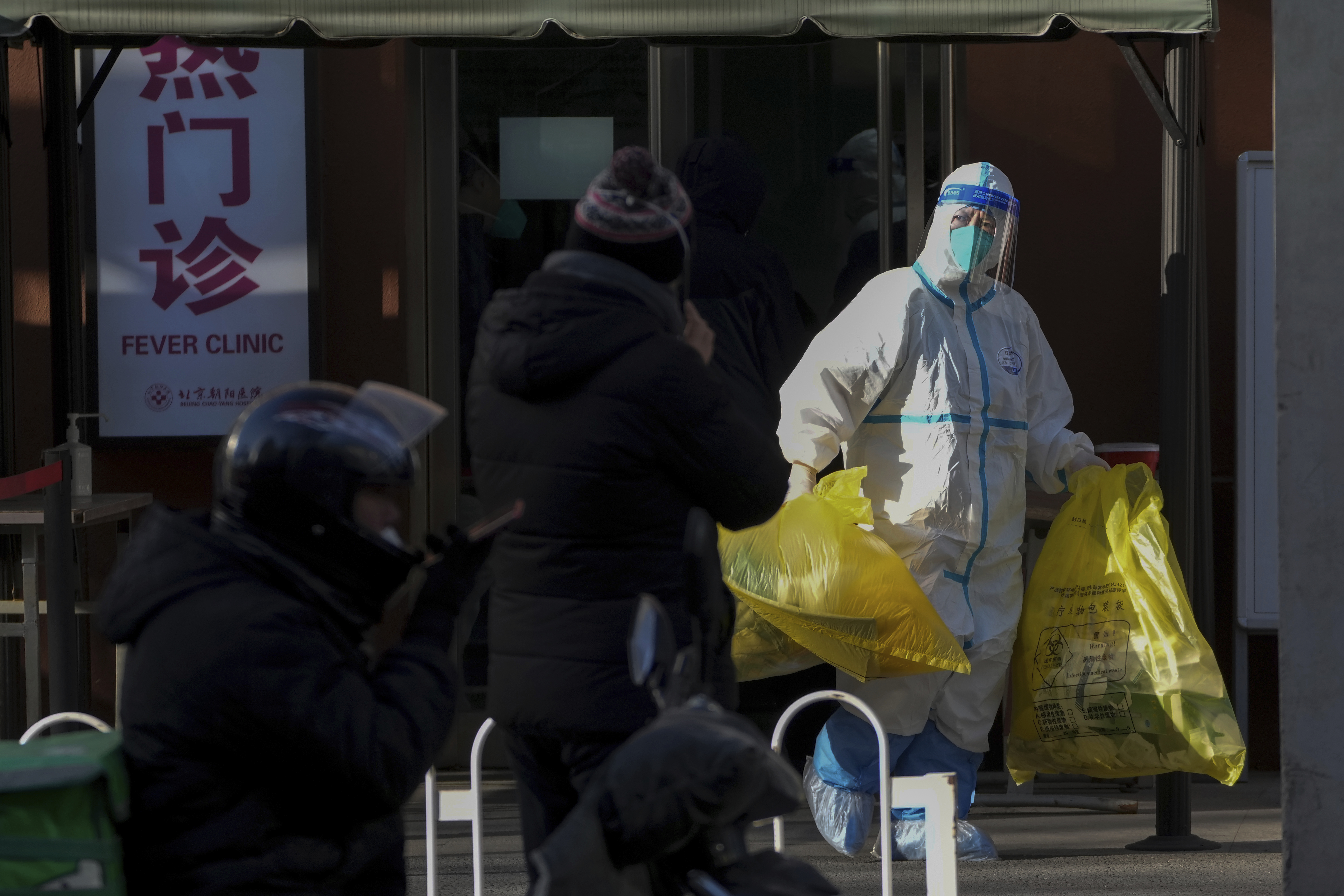 A medical worker in protective gear carries yellow bags of medical waste from a fever clinic in Beijing, Monday, Dec. 19, 2022. 