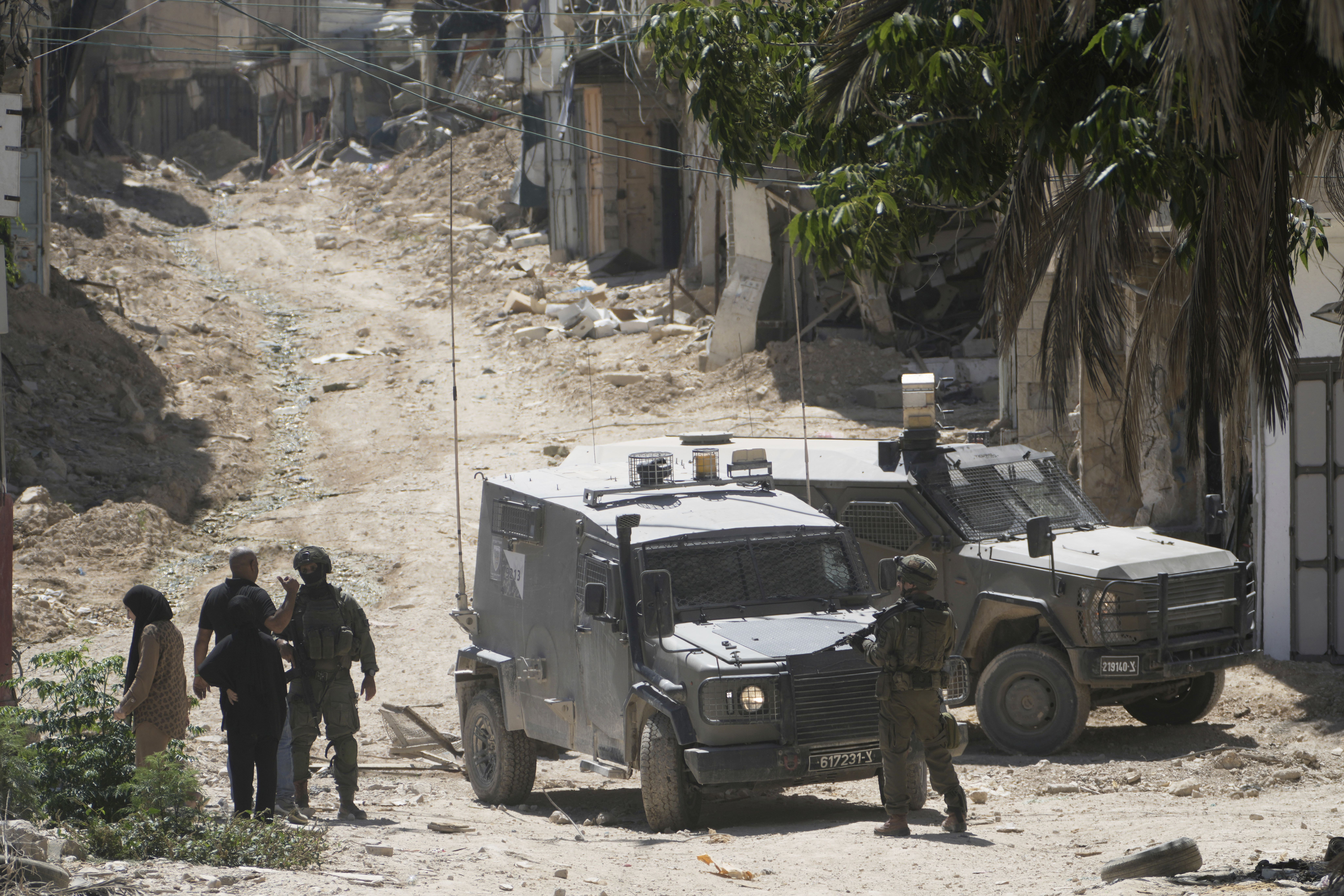 Israeli soldiers speak with Palestinians in the West Bank urban refugee camp of Tulkarm while residence evacuate their homes and carry their belongings as the Israeli military continues its operation in the area ahead of planned home demolitions by Israeli security forces, Sunday, July 6, 2025. (AP Photo/Majdi Mohammad)