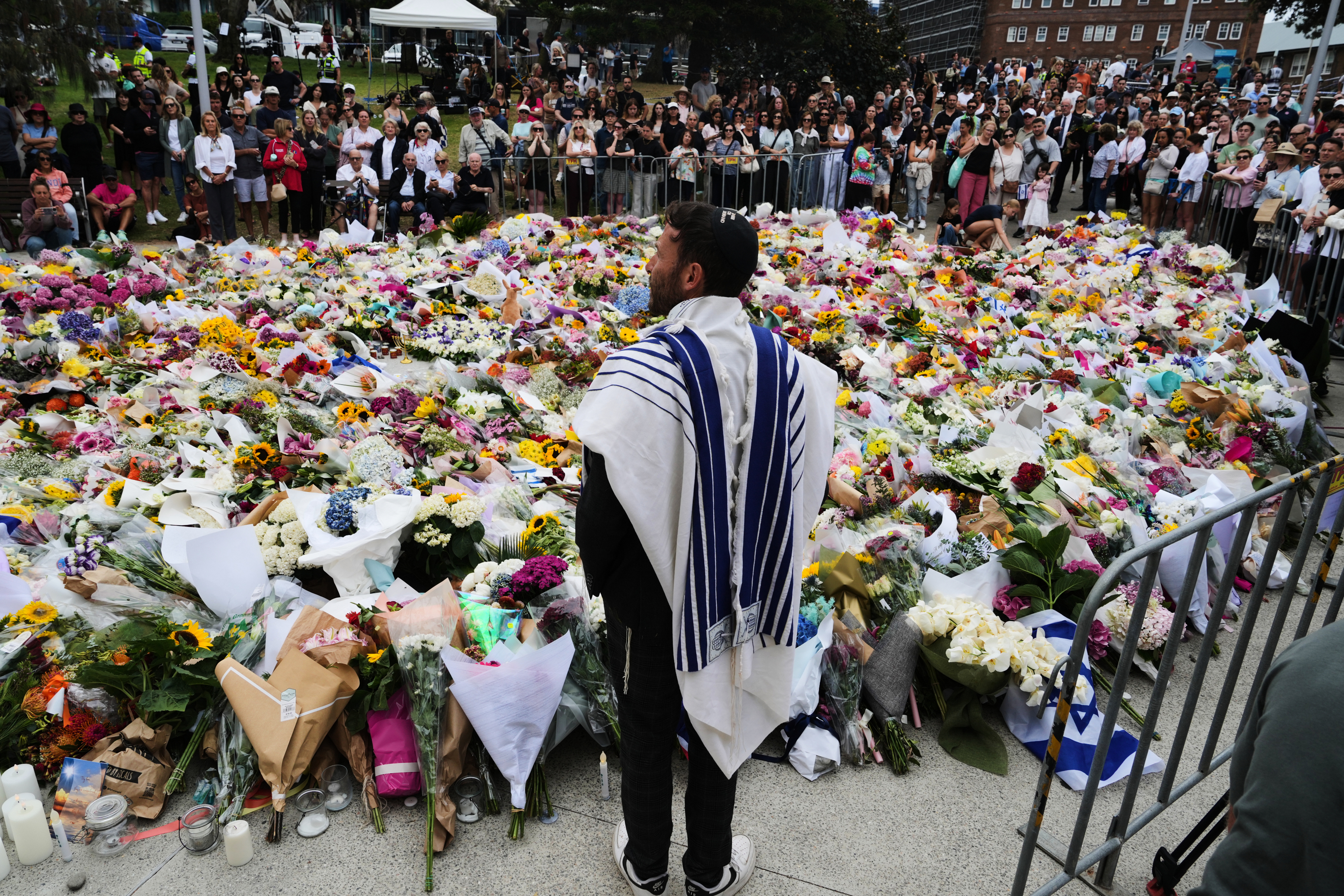 Rabbi Yossi Friedman speaks to people gathering at a flower memorial by the Bondi Pavilion at Bondi Beach.