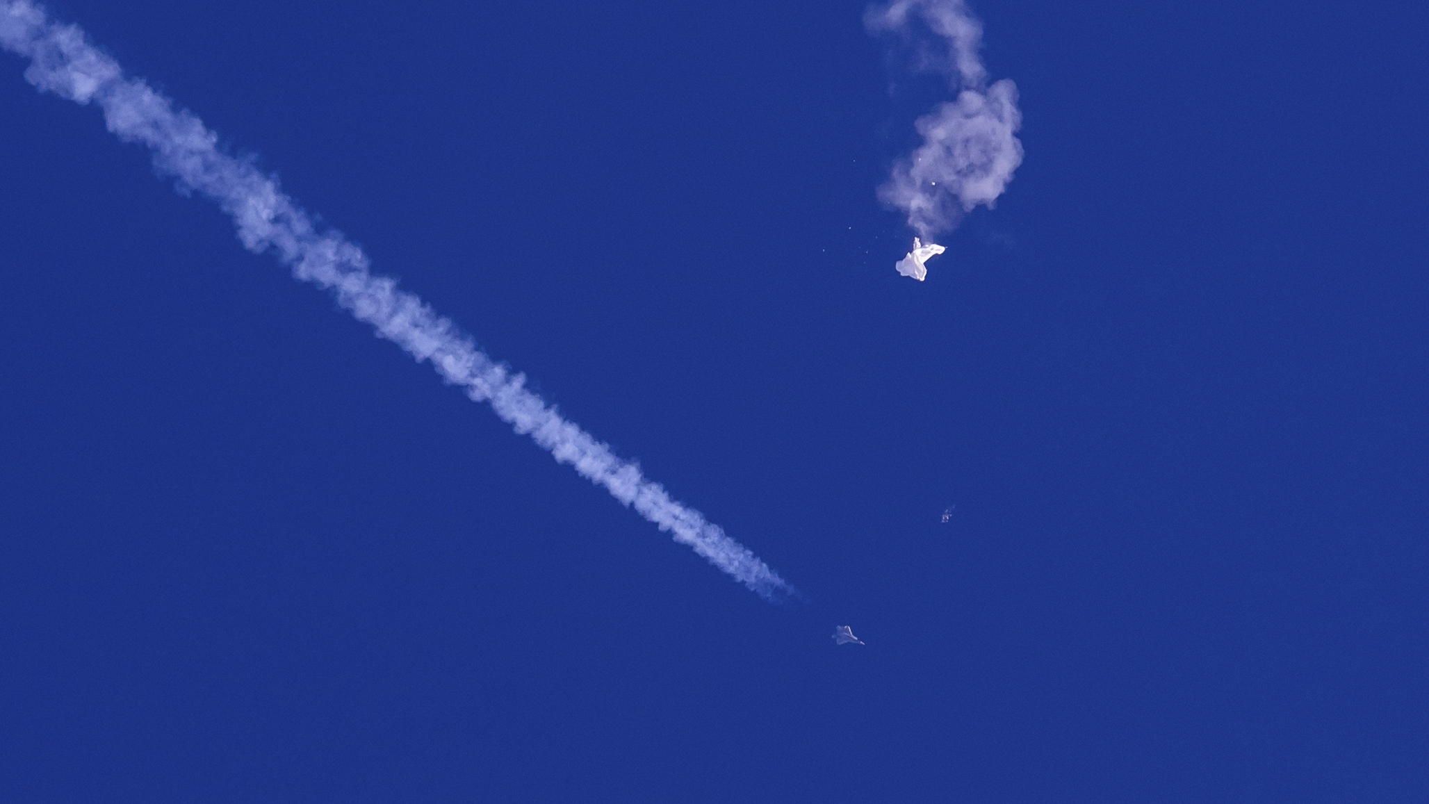 En esta foto proporcionada por Chad Fish, los restos de un gran globo flotan sobre el Océano Atlántico, frente a la costa de Carolina del Sur, con un avión de combate y su estela debajo.