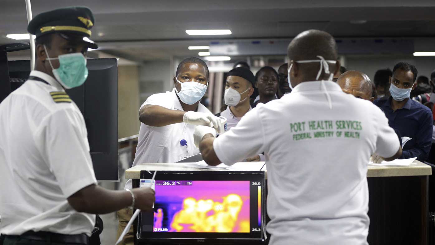 A Nigerian port health official, right, uses a thermometer to screen Ethiopian Airline cabin crews for COVID-19 virus.