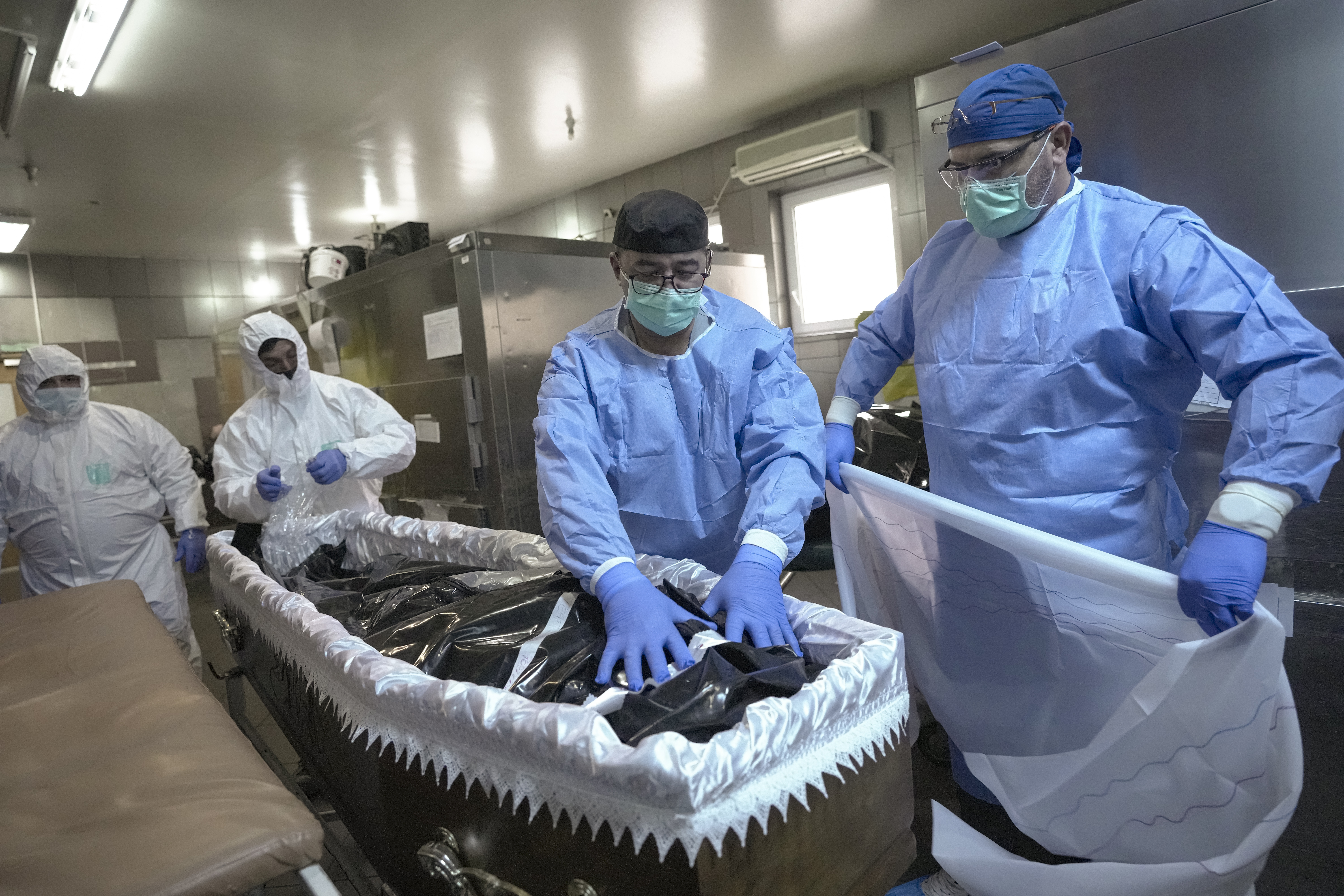 Members of the medical staff place the body of a COVID-19 victim in a coffin together with funeral house employees at the University Emergency Hospital morgue in Bucharest, Romania. 