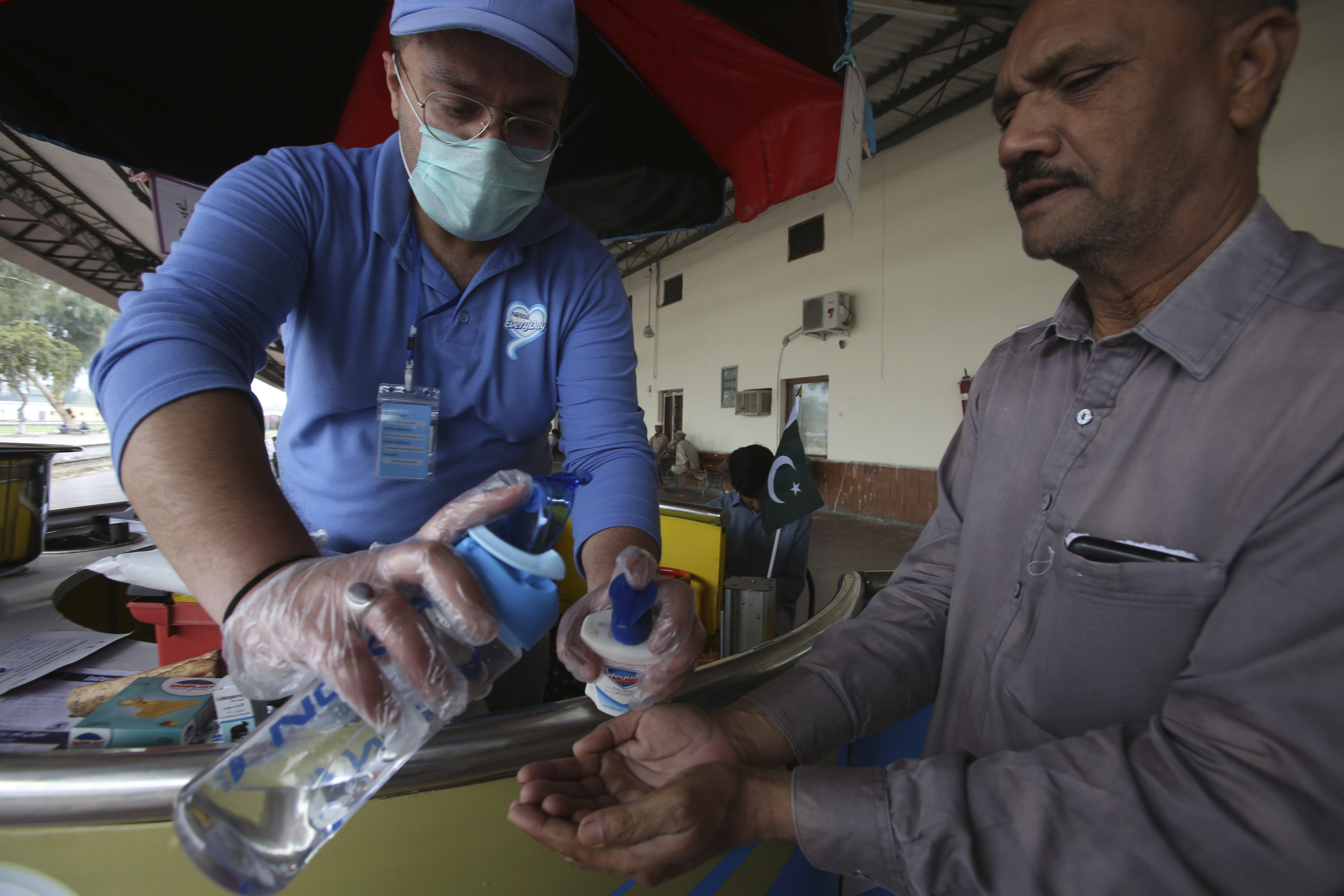 A Pakistani volunteer helps a passenger arriving at a railway station to wash hands as a measure to help prevent the spread of the coronavirus.