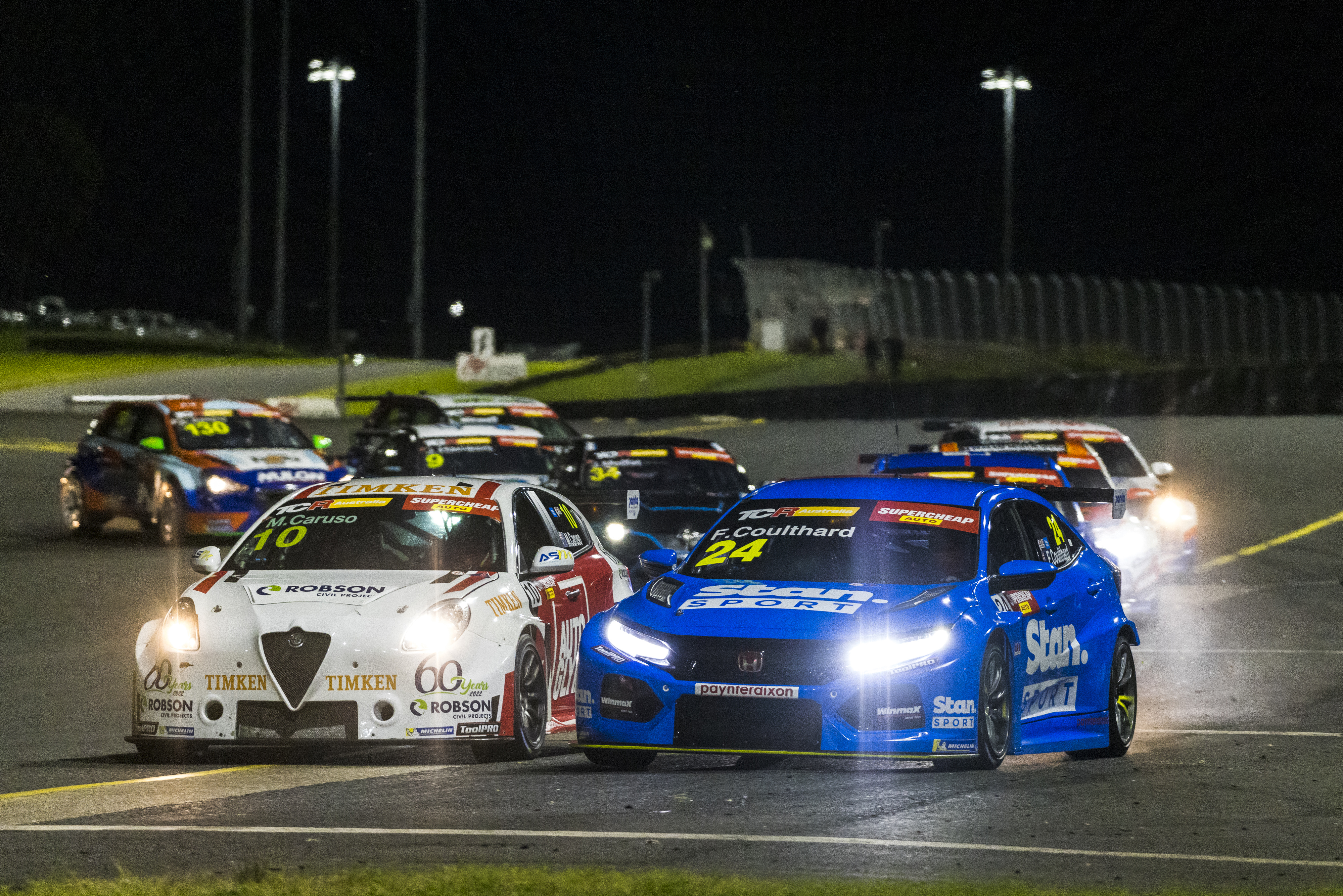Michael Caruso and Fabian Coulthard race side-by-side under lights at Sydney Motorsport Park.