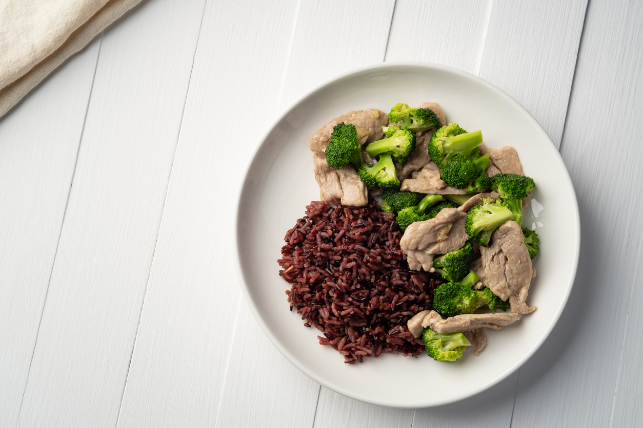 Cooked riceberry rice and Stir fried broccoli with pork tenderloin fillet in white plate.