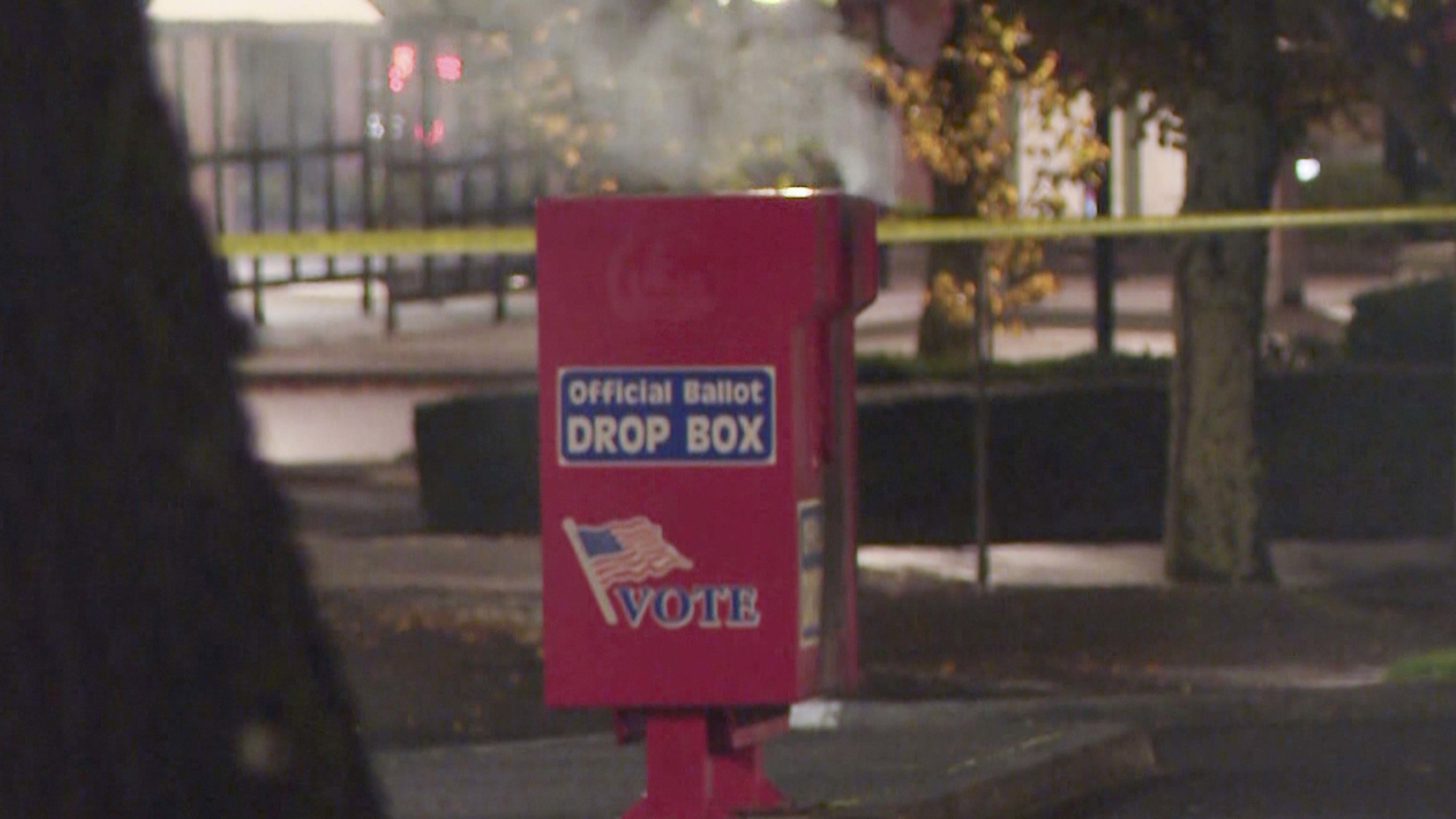 In this image made from a video provided by KGW8, authorities investigate the scene as smoke pours out of a ballot box on Monday, Oct. 28, 2024, in Vancouver, Wash. (KGW8 via AP)