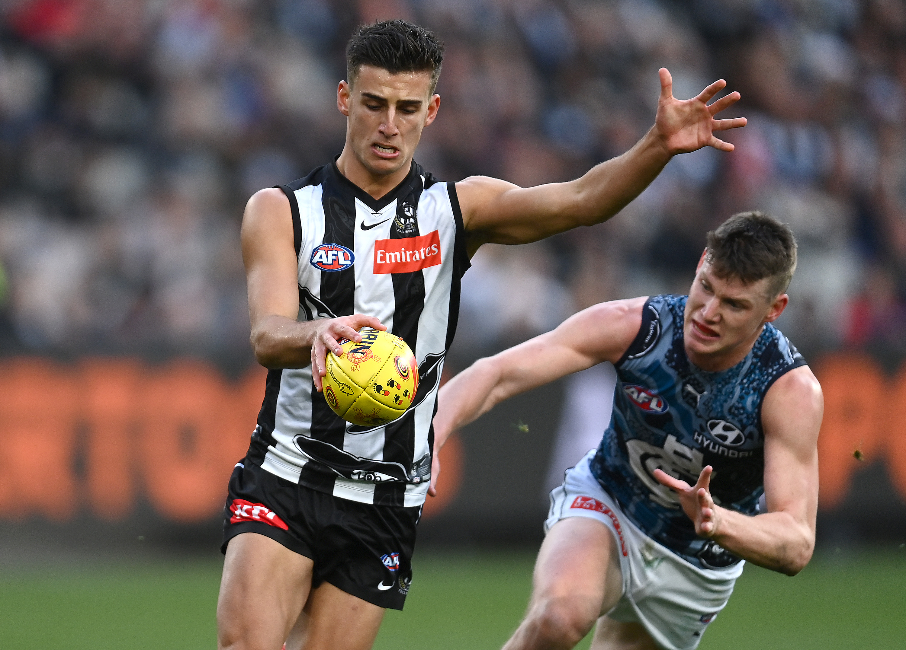 Nick Daicos kicks whilst being tackled by rival Sam Walsh.