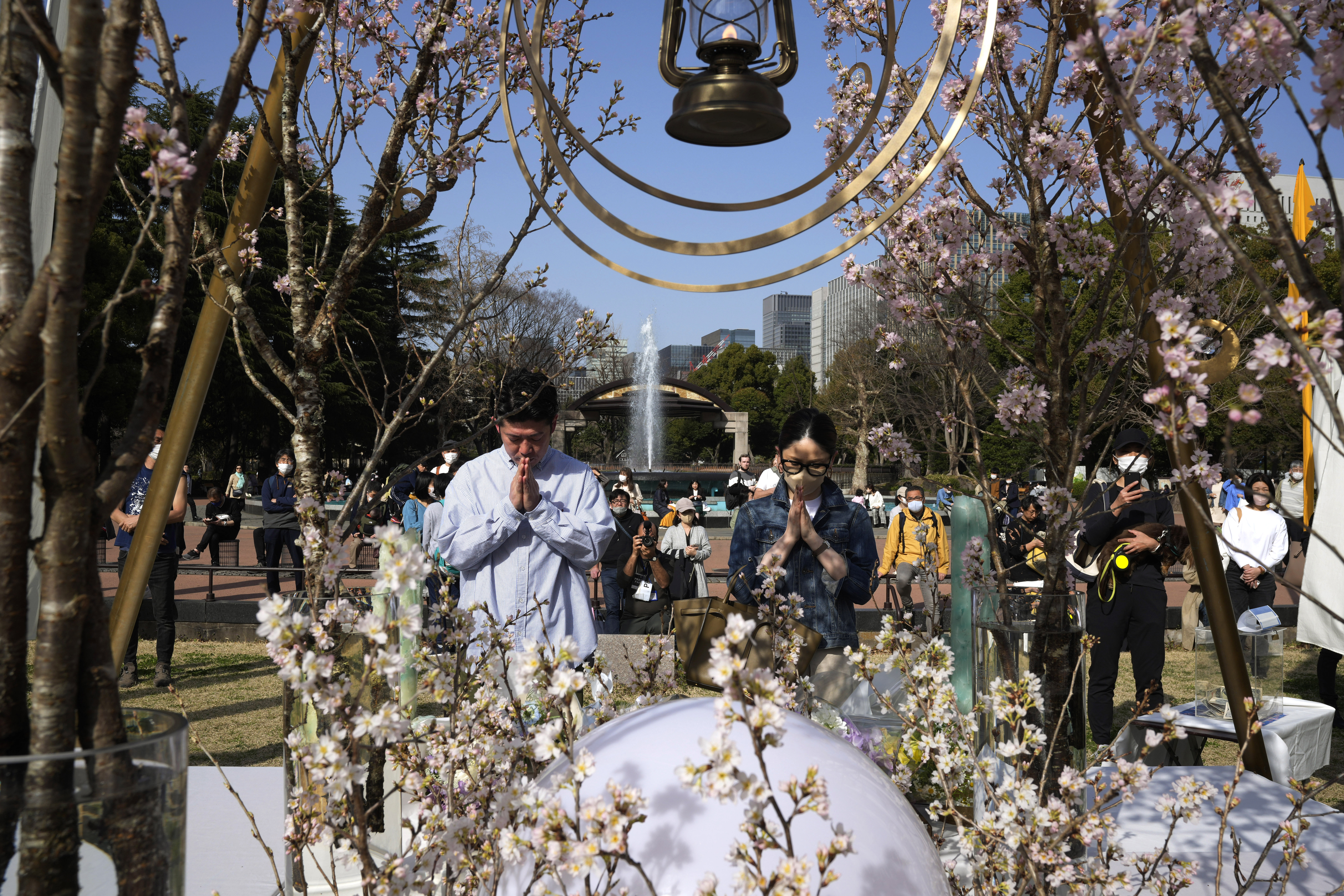 A man and a woman pray after laying flowers in front of a memorial set up to mark the 12th anniversary of the massive earthquake, tsunami and nuclear disaster, at Hibiya Park in Tokyo, Saturday, March 11, 2023