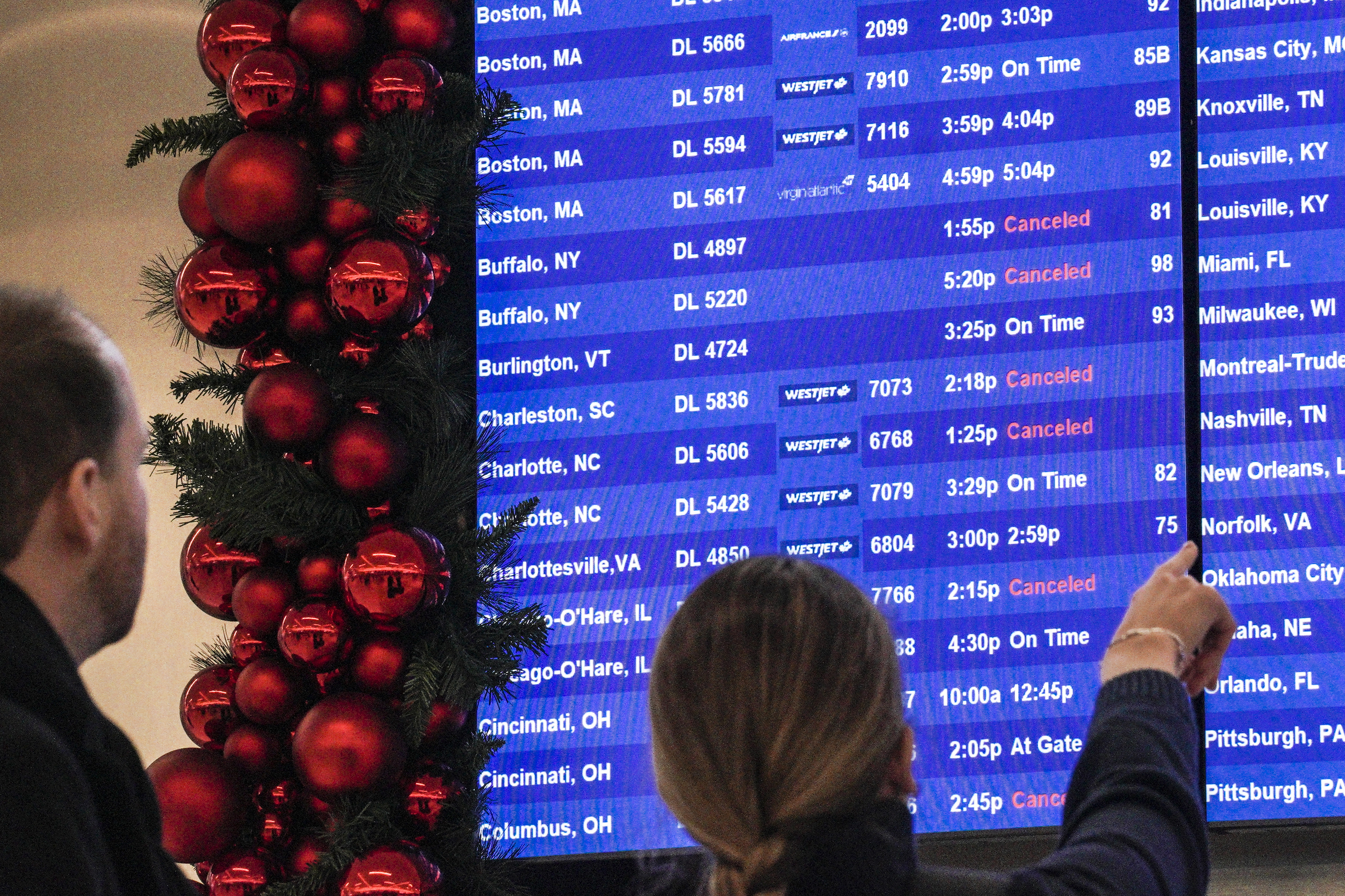Passengers check flight departure schedule, some showing cancellations, as they arrive at the Delta terminal at Laguardia Airport, Friday Dec. 23, 2022, in New York. (AP Photo/Bebeto Matthews)