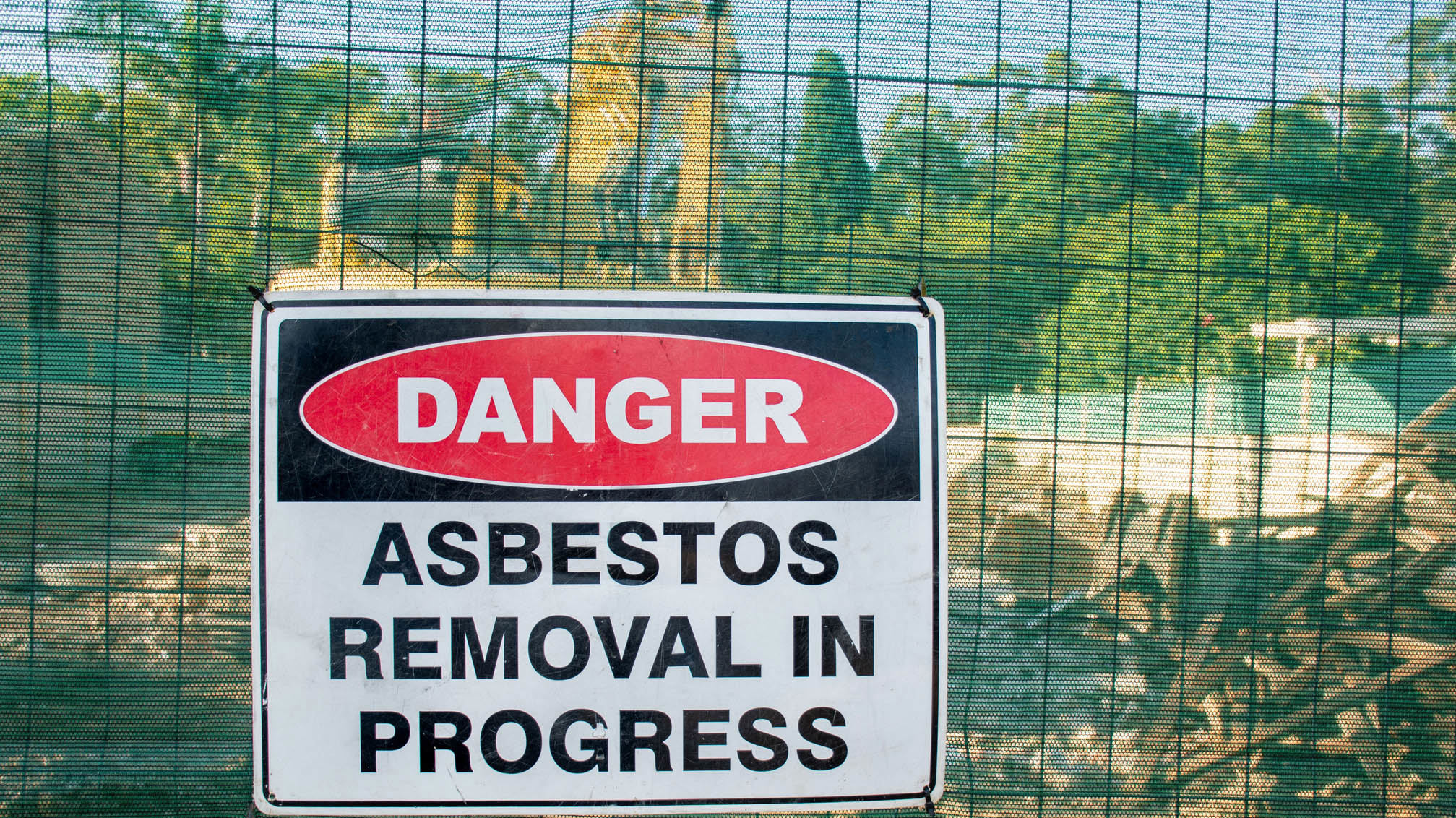 A warning sign Danger Asbestos on a fence at construction site where old house is demolishing