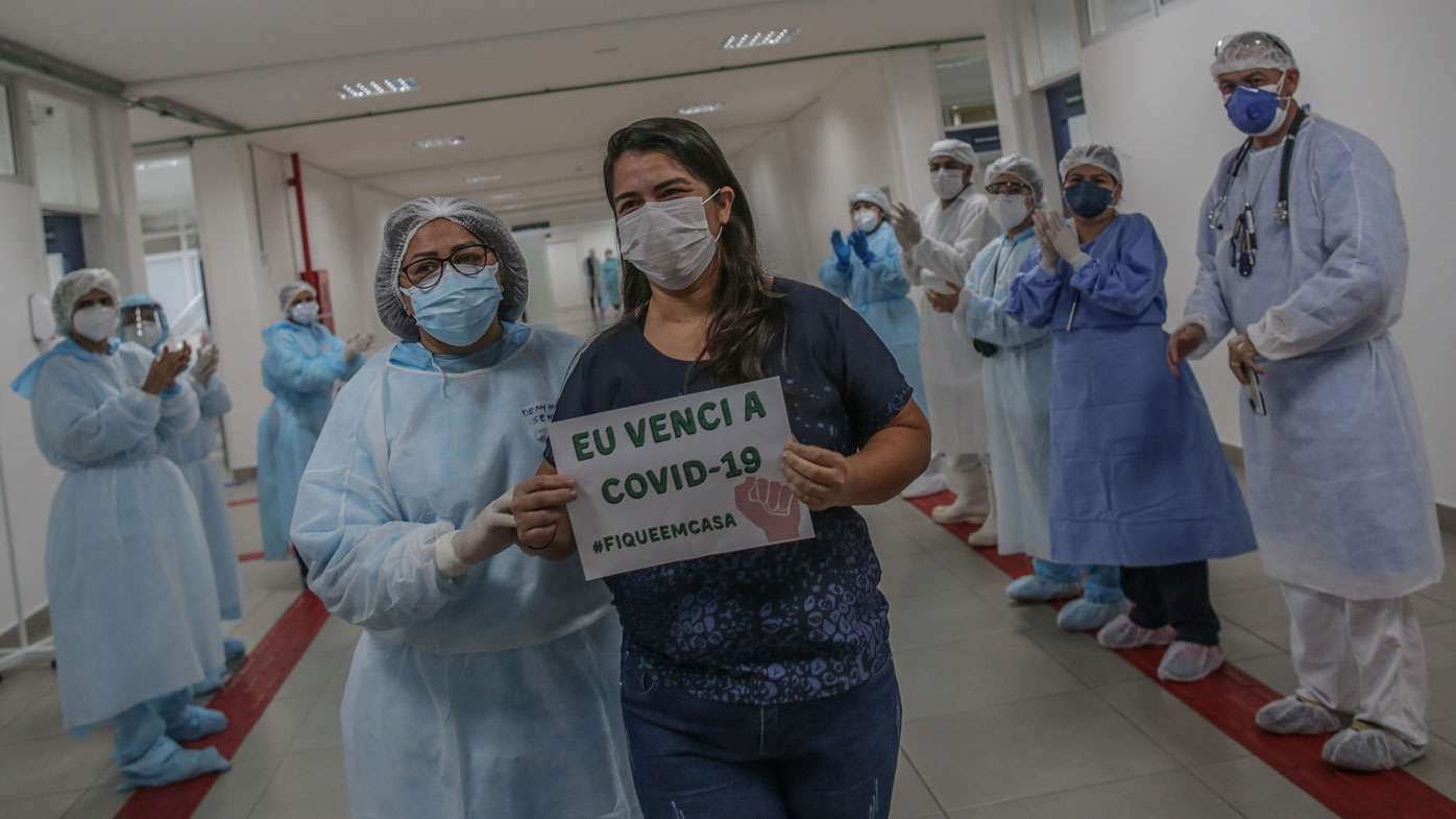 After 10 days of treatment for coronavirus, Kelly Araujo de Andrade holds a sign that reads "I beat the COVID-19 #StayAtHome" while she walks through the main hall followed by a chief nurse leaving the Gilberto Novaes Municipal Field Hospital, in Manaus, Brazil.