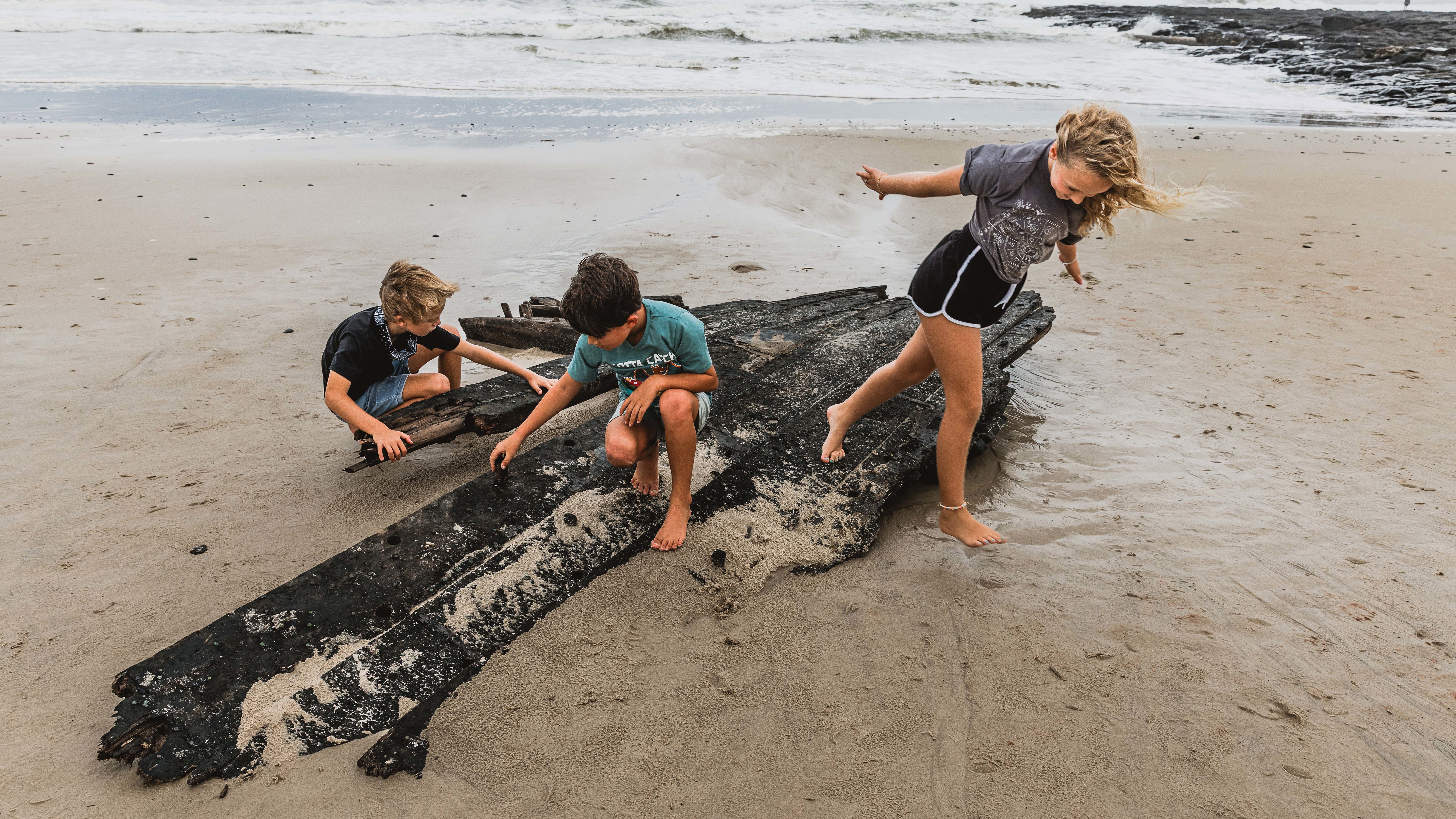 Ex-Cyclone Alfred has unearthed what is believed to be part of historic ship The Comet on a Ballina Beach. Photo shows Ocsar Pllo, Axel Doherty and Daisy Plooy playing by it. 