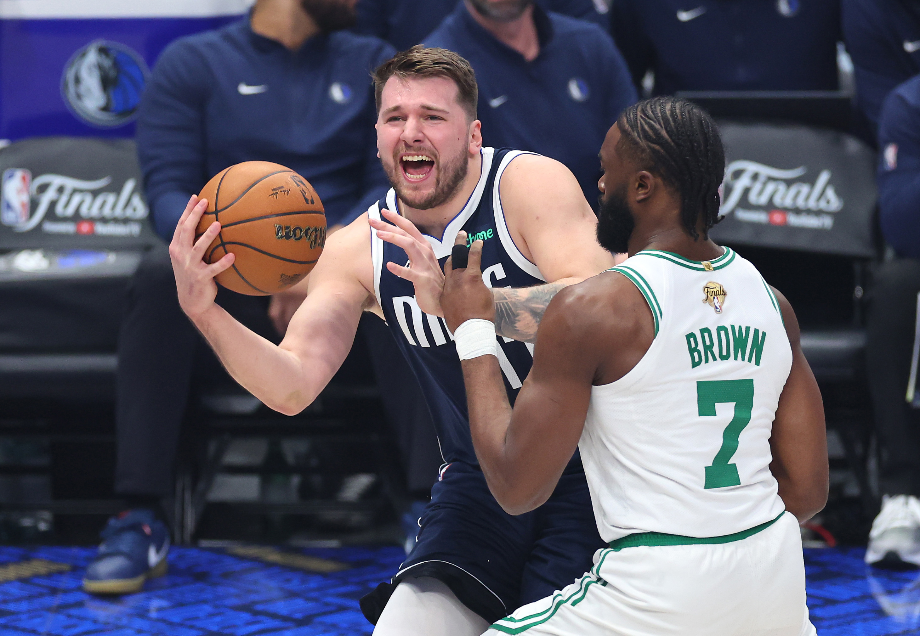 Luka Doncic of the Dallas Mavericks dribbles while being fouled by Jaylen Brown of the Boston Celtics.