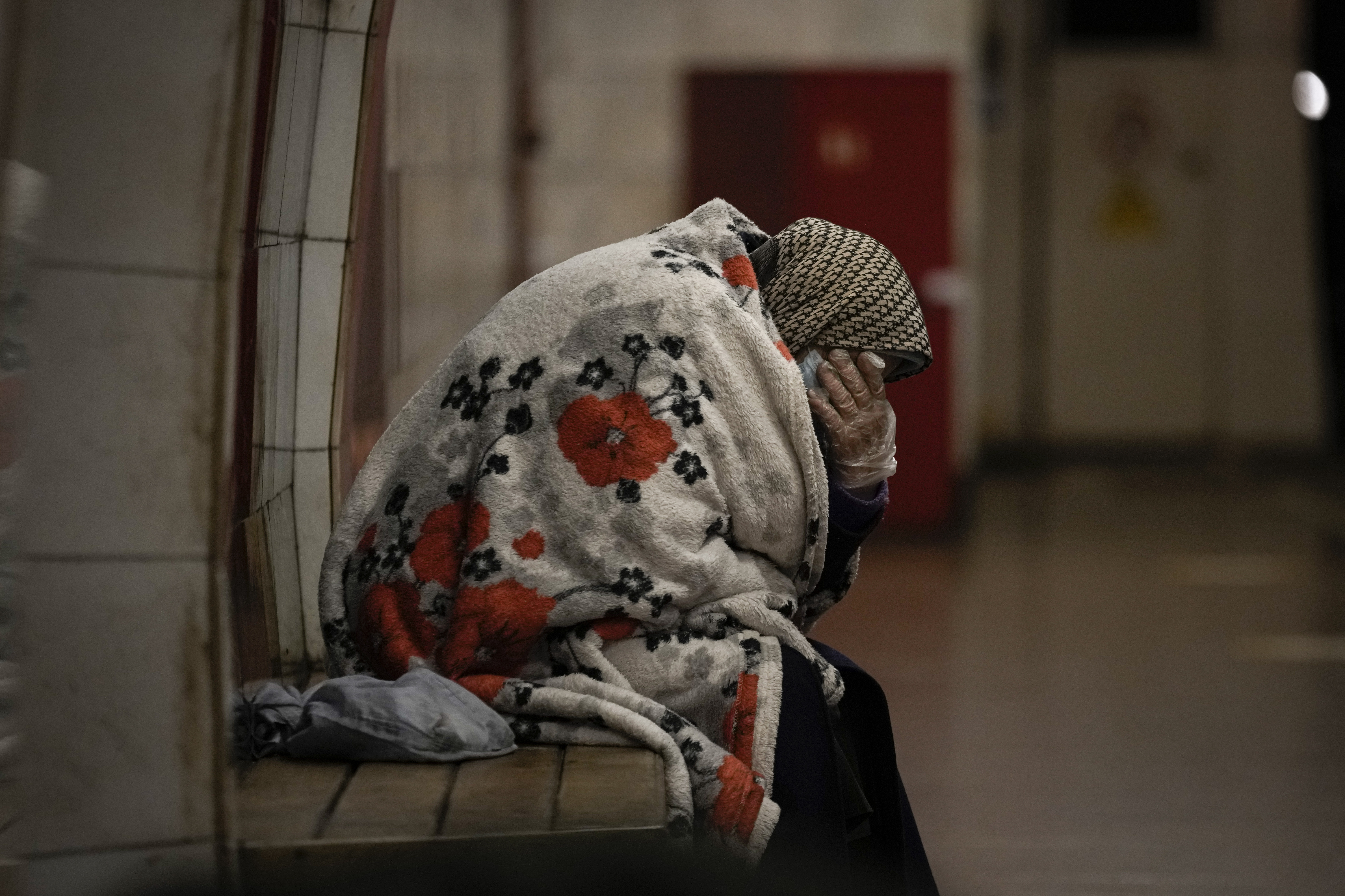 An elderly woman sits on a bench wrapped in a blanket in a subway station turned into a shelter in Kyiv, Ukraine, Tuesday, March 8, 2022.