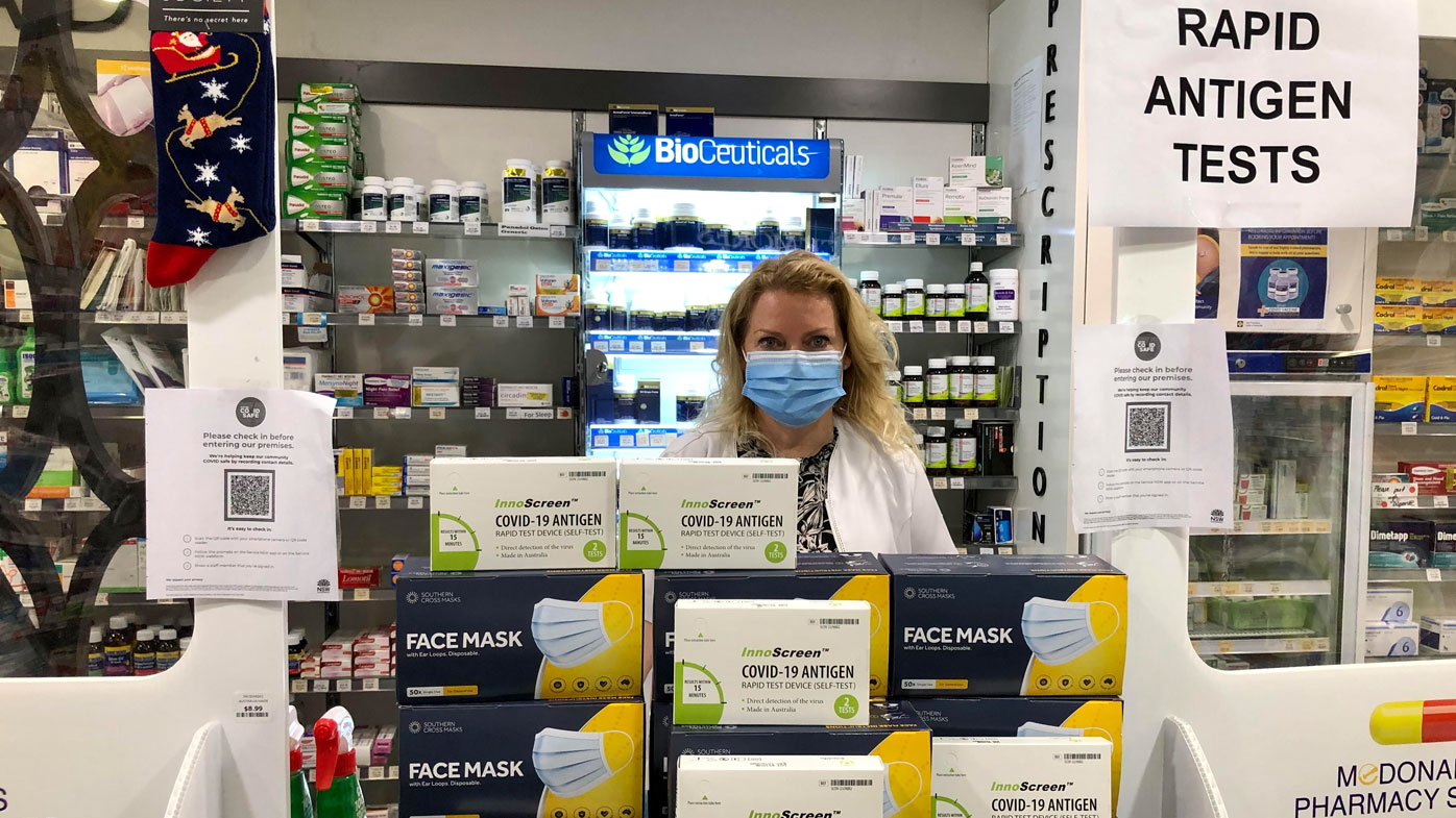A Sydney pharmacist stands near the counter, where a sign advertises rapid antigen tests for sale.
