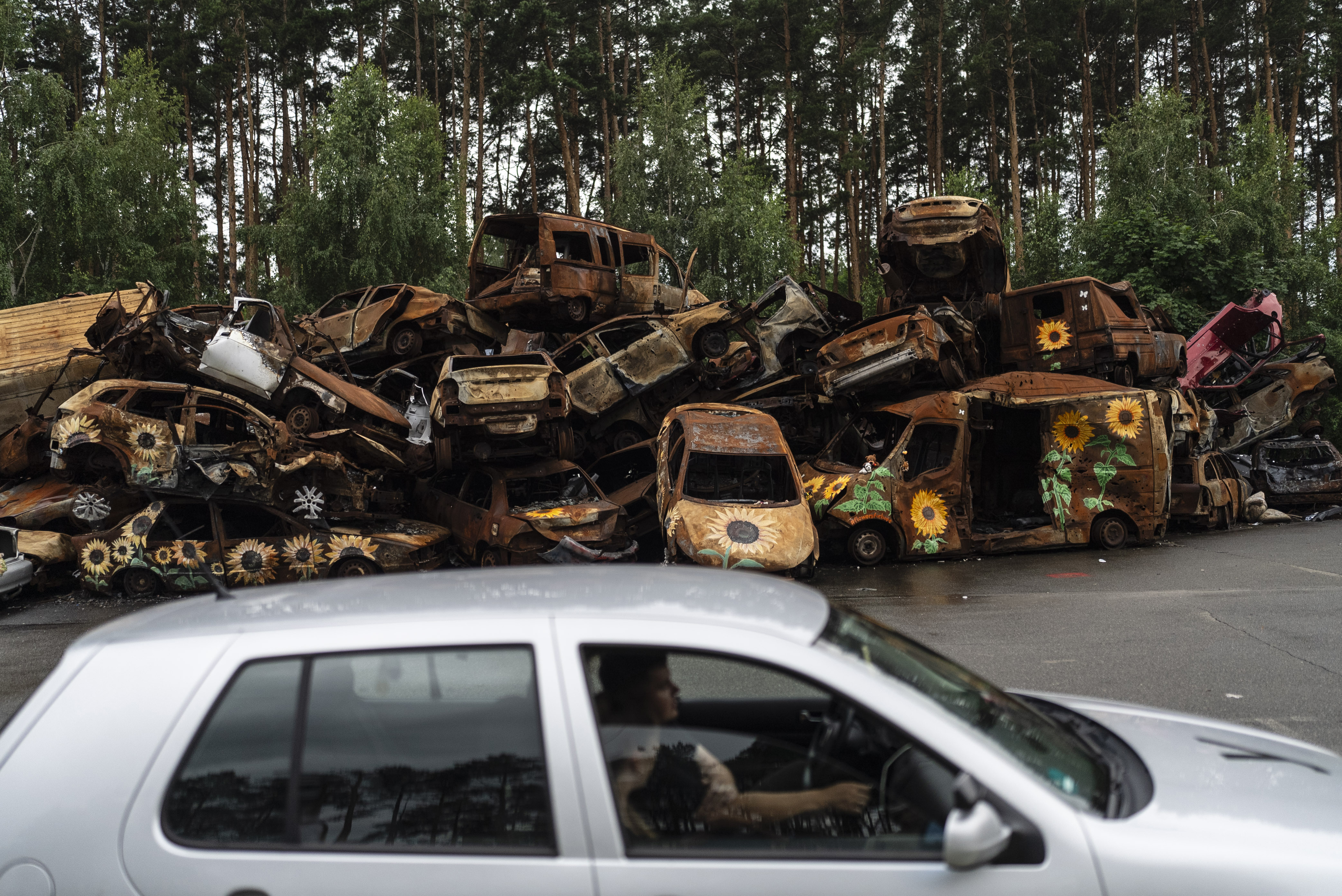 Los vehículos destruidos por los ataques rusos se apilan en un lote mientras un instructor de manejo, en primer plano, habla con su estudiante de manejo en Irpin, Ucrania.