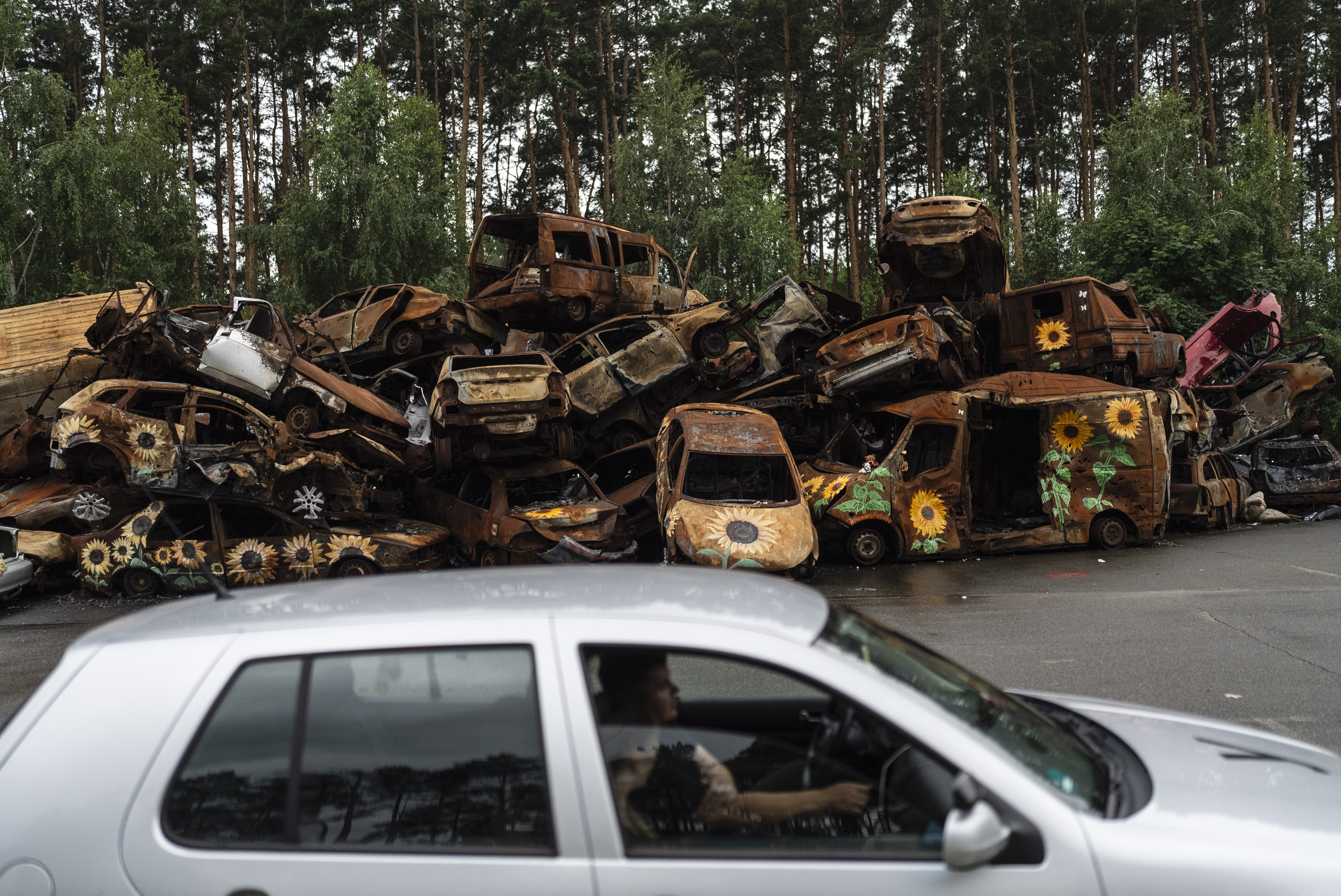 Vehicles destroyed by Russian attacks are piled up in a lot as a driving instructor, foreground, talks to his student driver in Irpin, Ukraine.