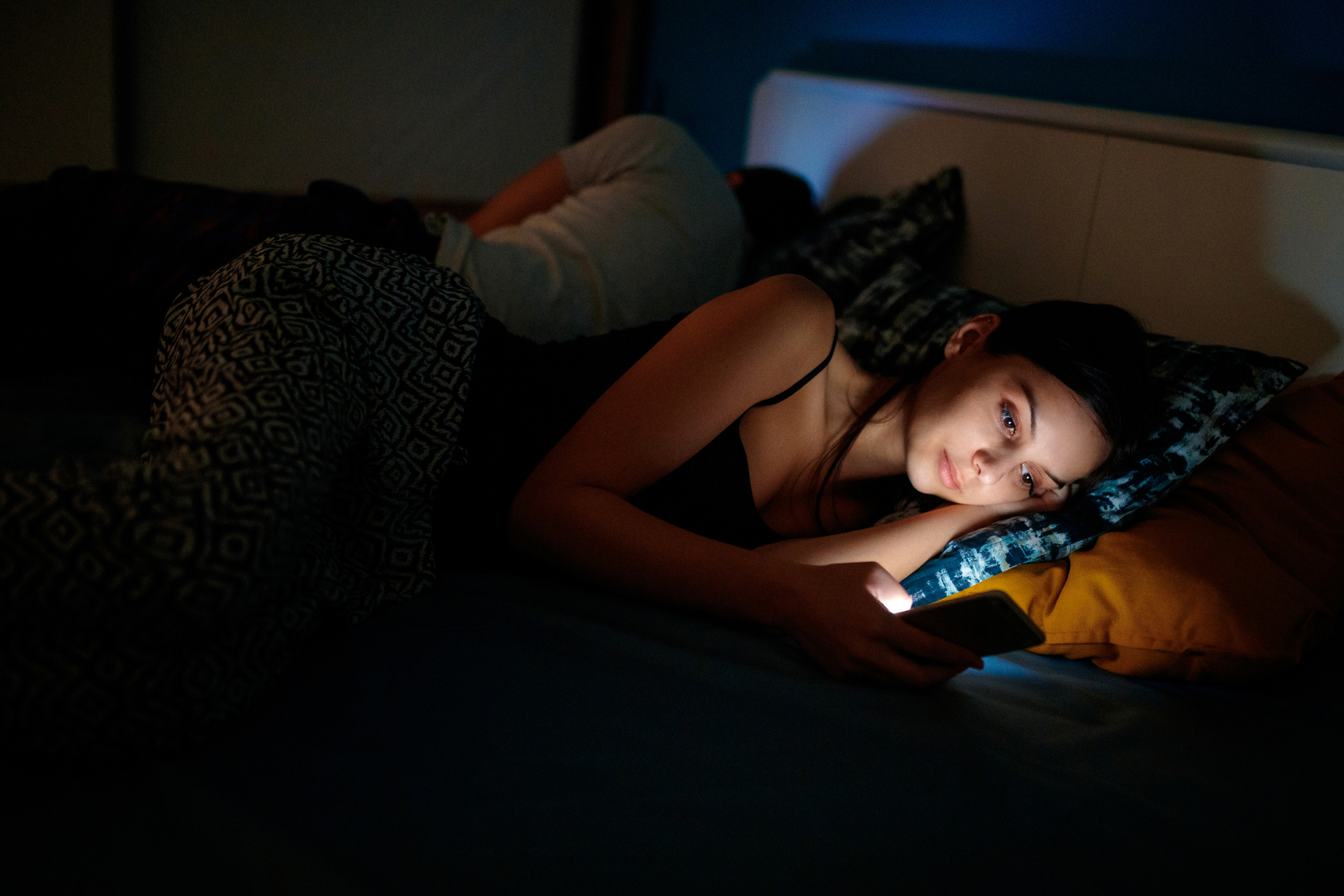 Young woman sending text message as her boyfriend sleeps in the bed