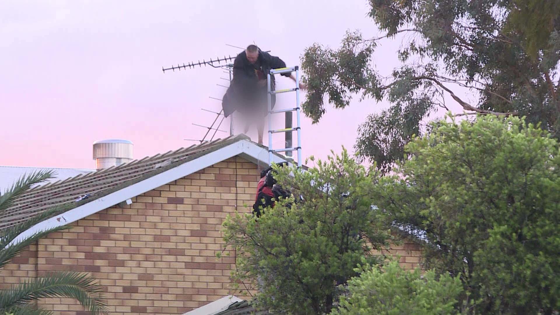 A man is under police guard after falling off the roof of a Tamworth home during a tense standoff with police. Peter Nielsen, 55, is accused of stabbing another man to death inside the home before climbing on top of the house.