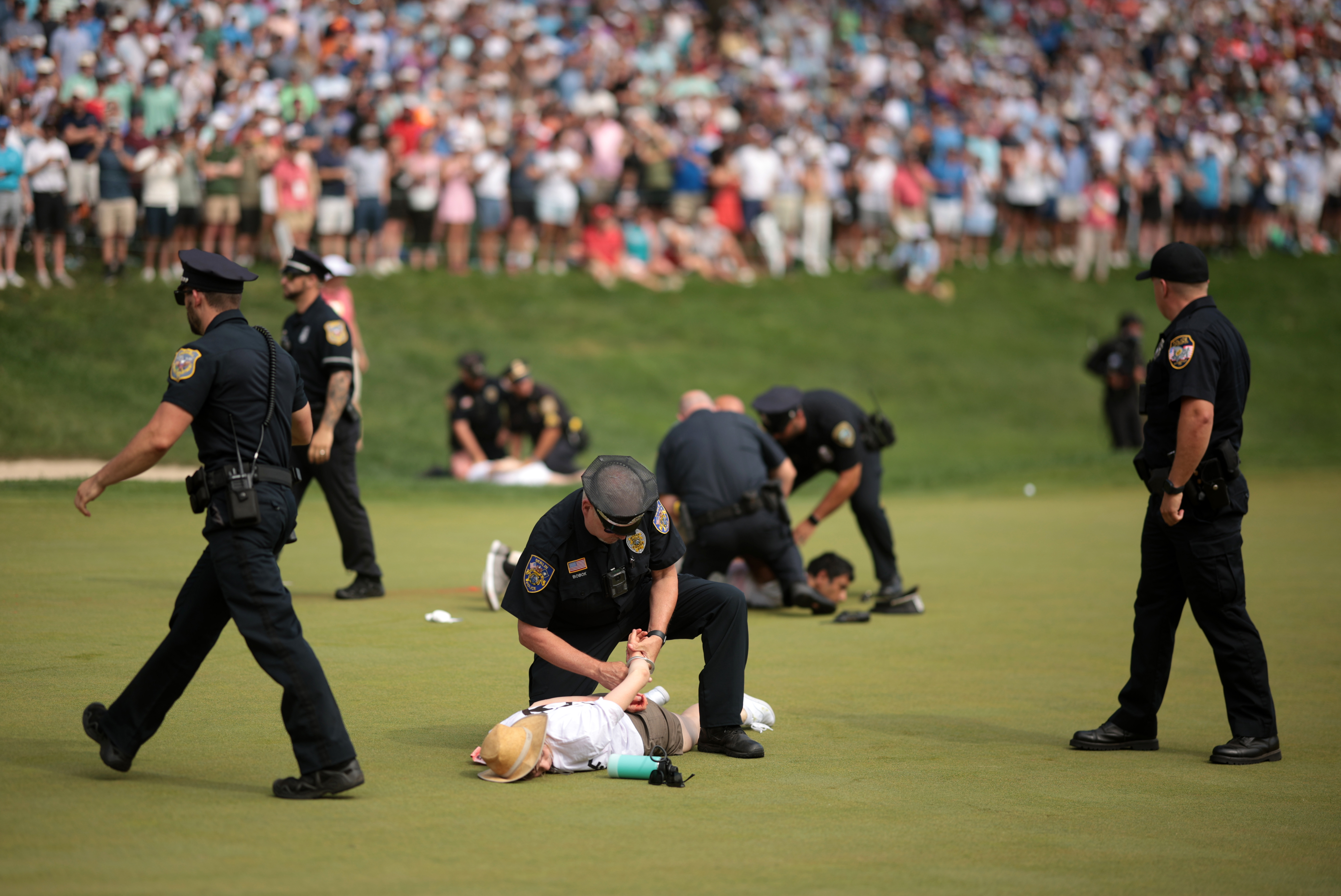 Climate protestors are ushered off the 18th green by police officers during the final round of the Travelers Championship.