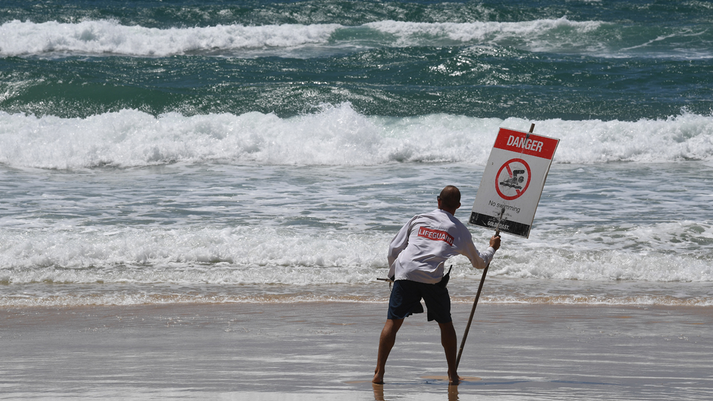 A lifeguard places a danger sign on a Gold Coast beach