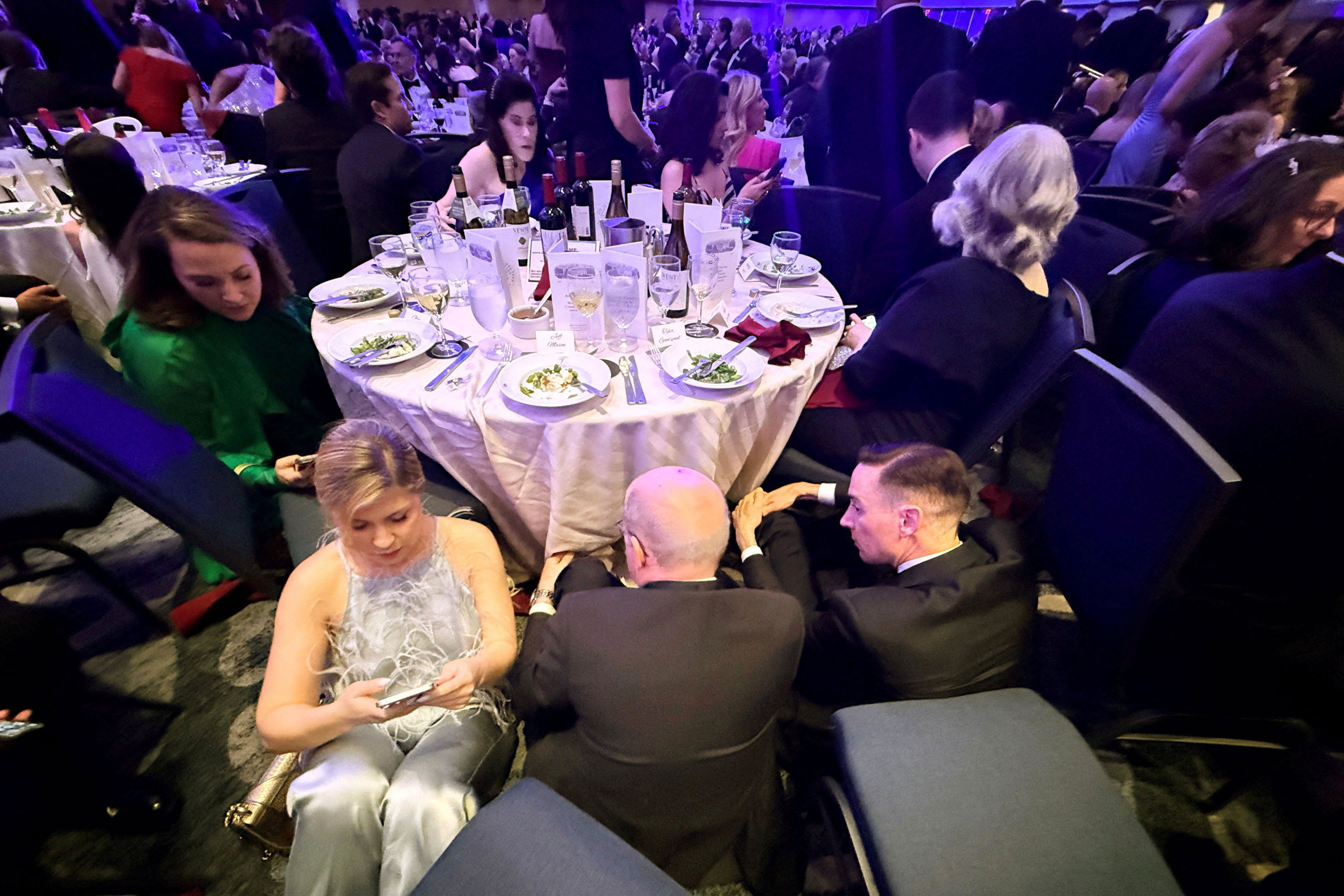 Guests take cover behind a table after US President Donald Trump and first lady Melania Trump were rushed out of the White House Correspondents' Association dinner by Secret Service agents.