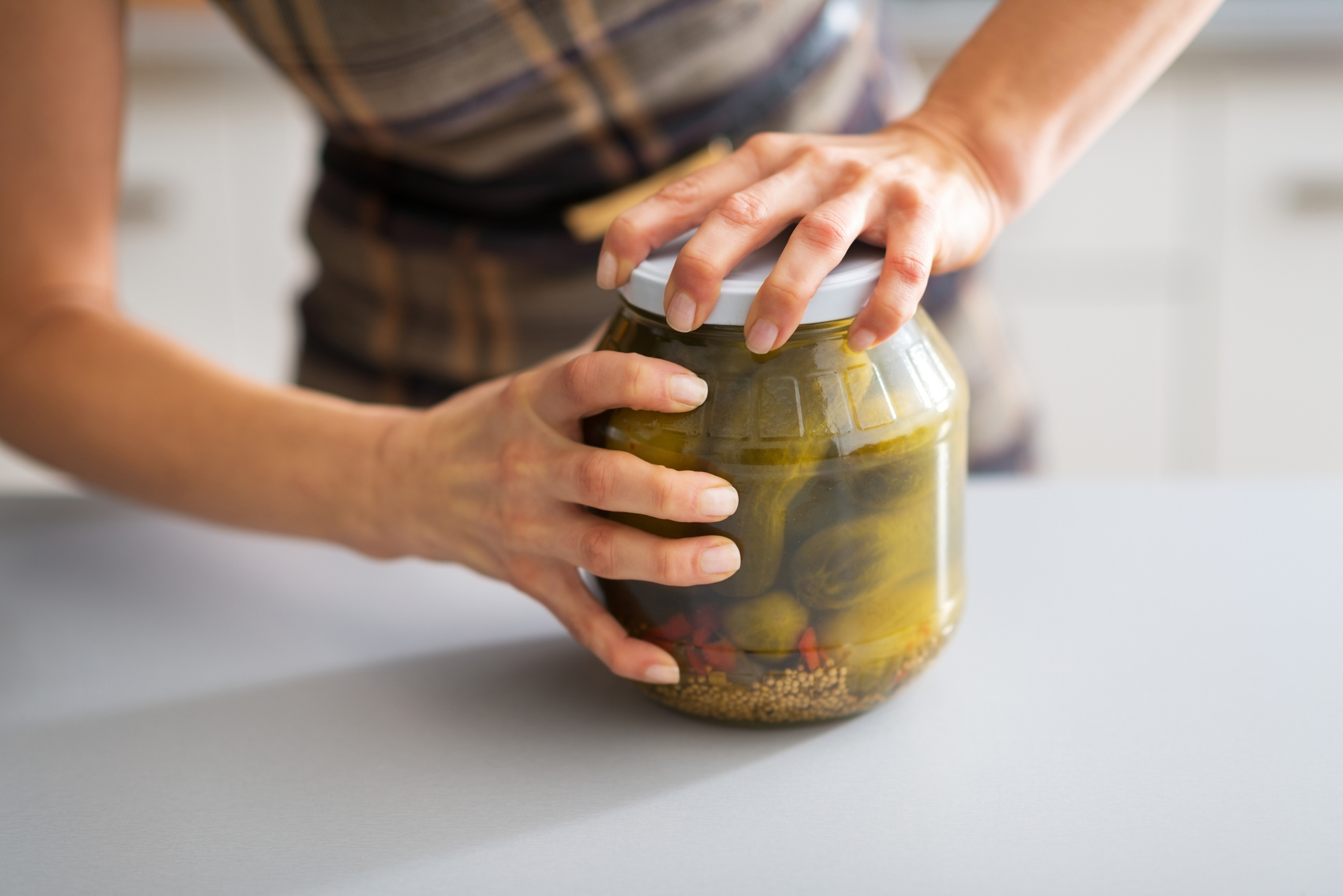 Stock photo of woman's hands opening jar of pickled cucumbers