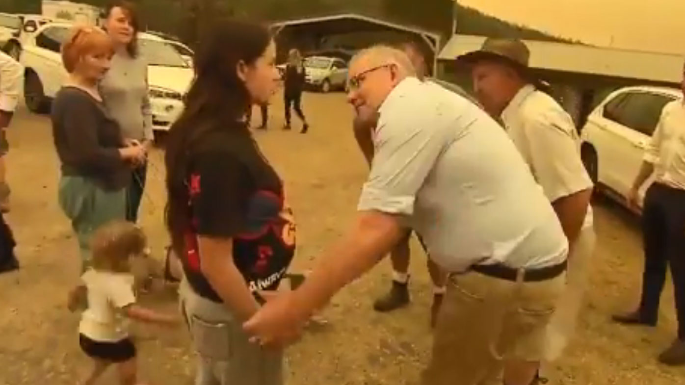 Scott Morrison takes a woman's hand to shake during his visit to Cobargo.