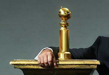 Imagen recortada de la mano del presentador de los Globos de Oro junto al trofeo (Getty)