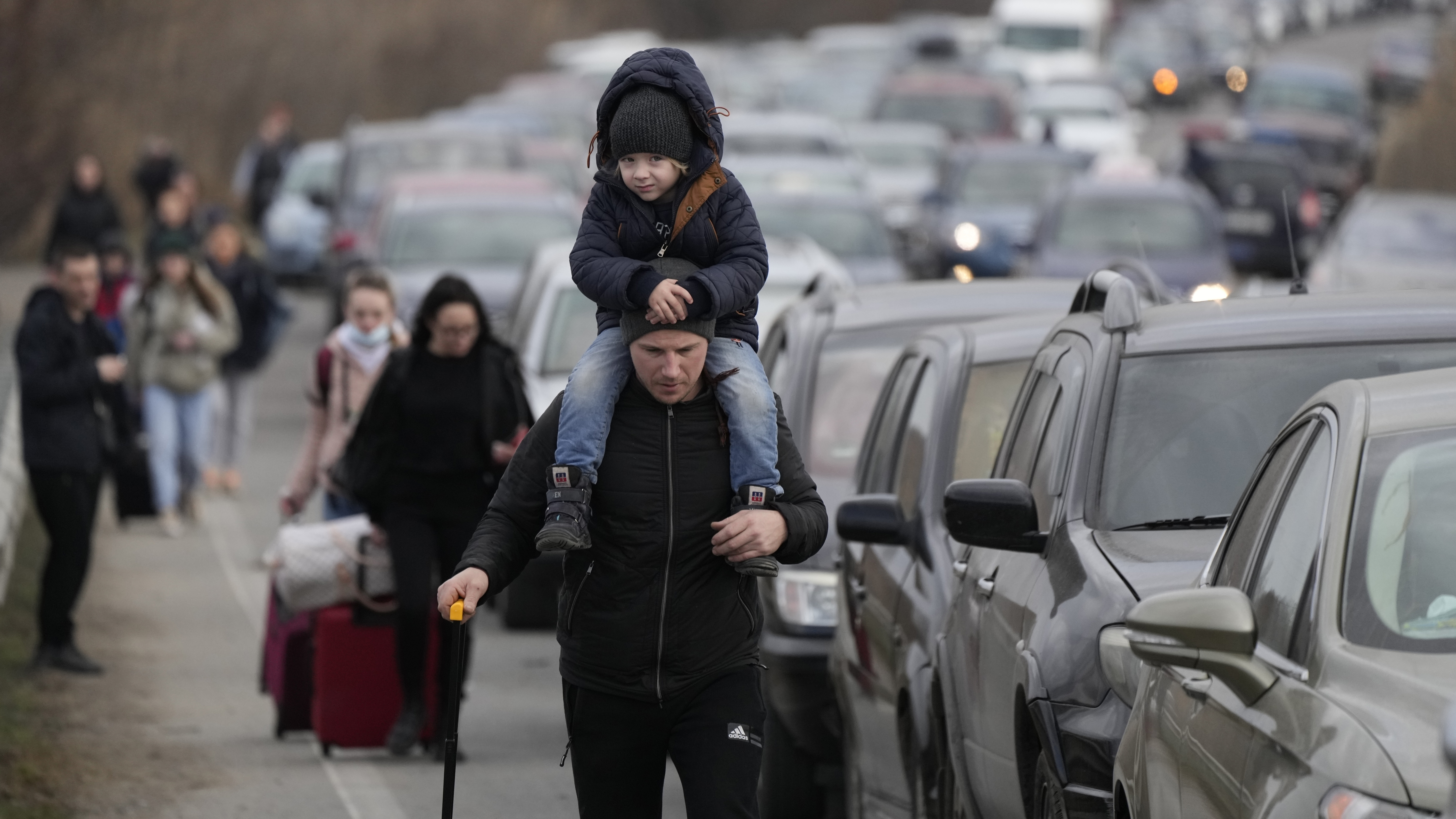 Ukrainian refugees walk along vehicles lining-up to cross the border from Ukraine into Moldova.