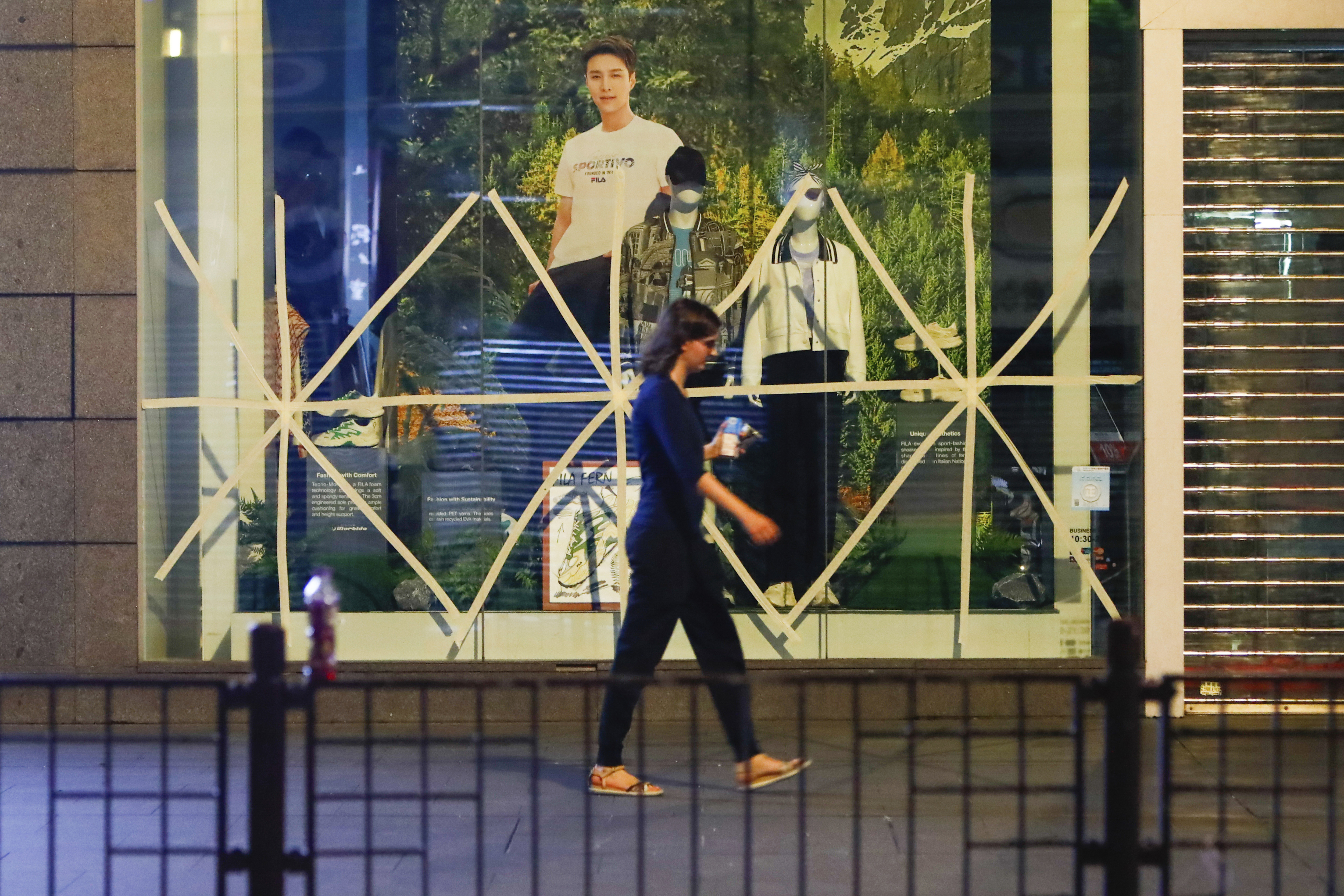 A woman walks past a fashion store with windows taped early in the morning, as a precaution against the approaching Super Typhoon Saola, in Hong Kong, on Friday, Sept. 1, 2023 