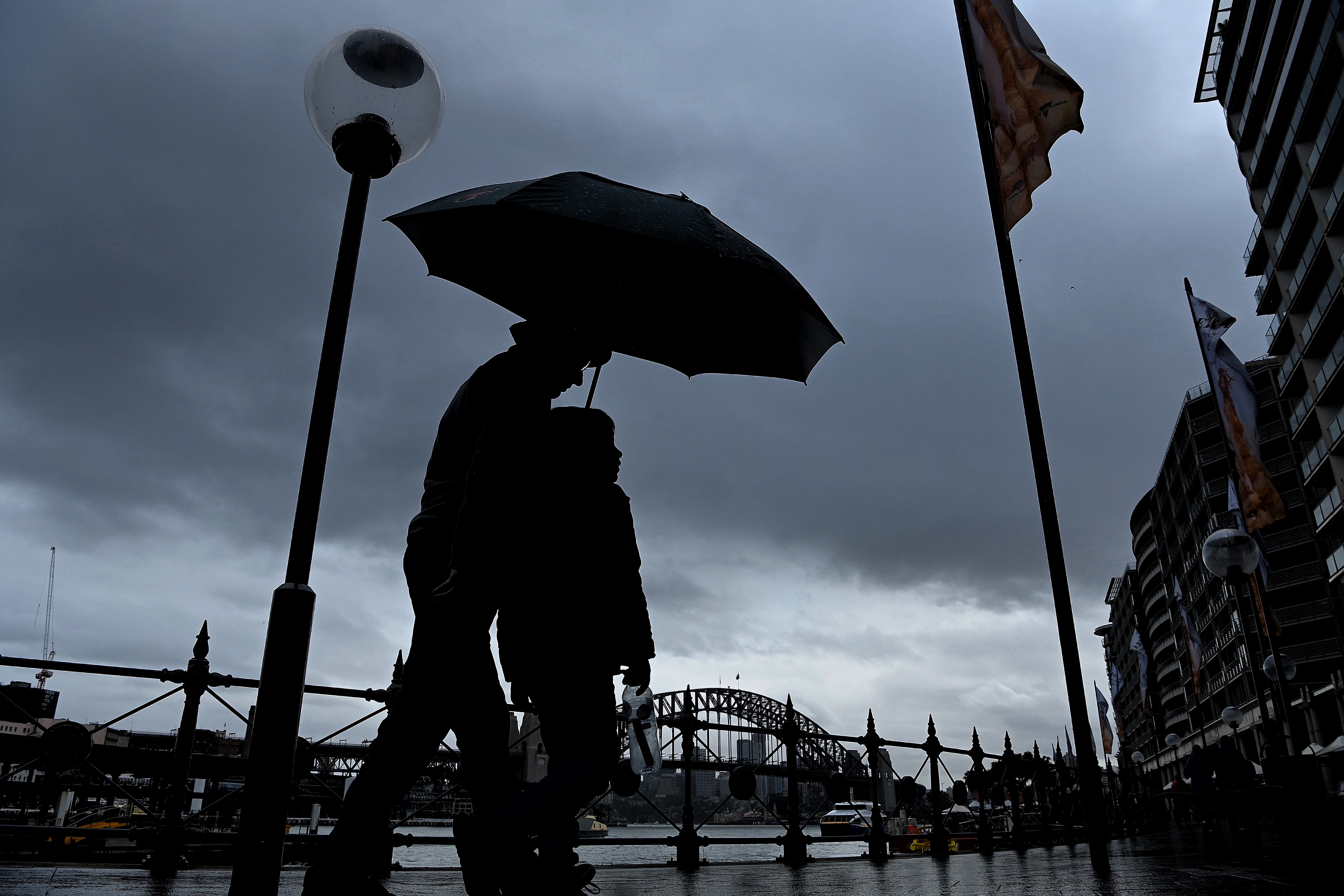 A man and child walk along Circular Quay shielding themselves from the rain with their umbrella. Sydney, NSW. 19th July, 2022. Photo: Kate Geraghty