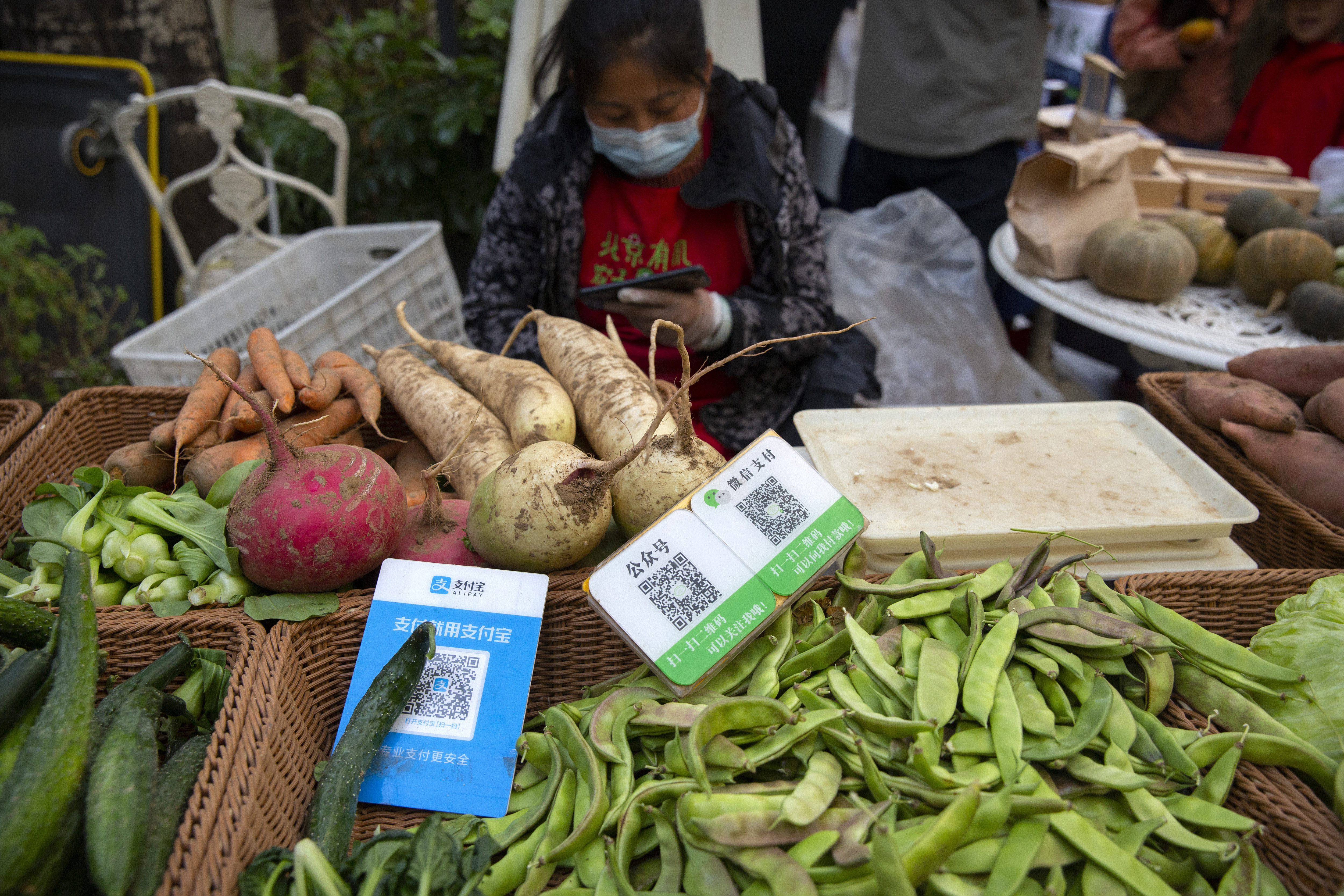 A vendor sits near cards displaying QR codes to pay electronically with WeChat Pay and Alipay at a farmer's market in Beijing